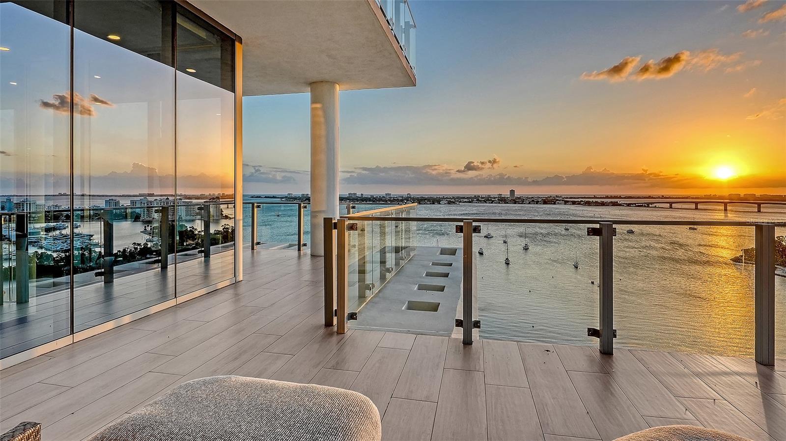 Condo balcony overlooking the bay and city skyline at sunset, with glass railings and tiled flooring.