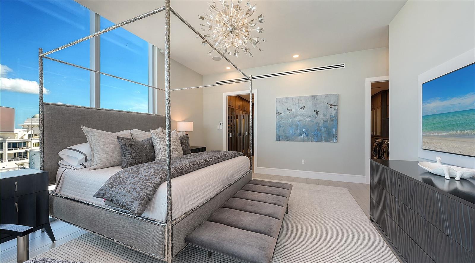 Contemporary bedroom with a gray canopy bed, floor-to-ceiling windows, and an upholstered bench.