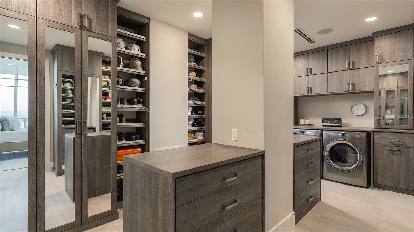 Walk-in closet and laundry room with a drawer island, shoe shelves, mirrored doors, and front-loading washer and dryer.