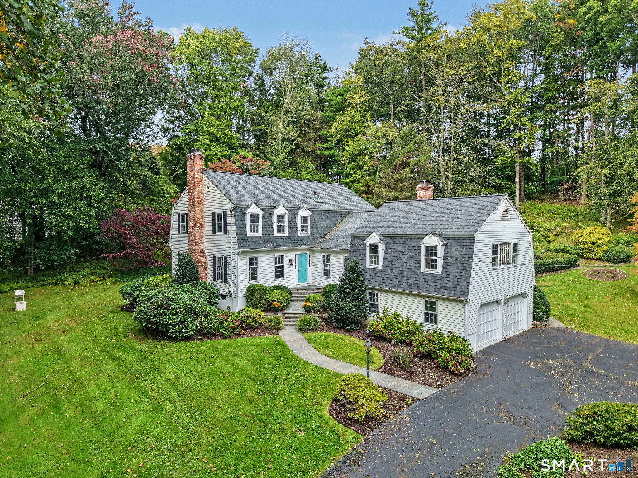 White clapboard home with gray dormer roofs, brick chimneys, landscaped gardens, and an attached garage.