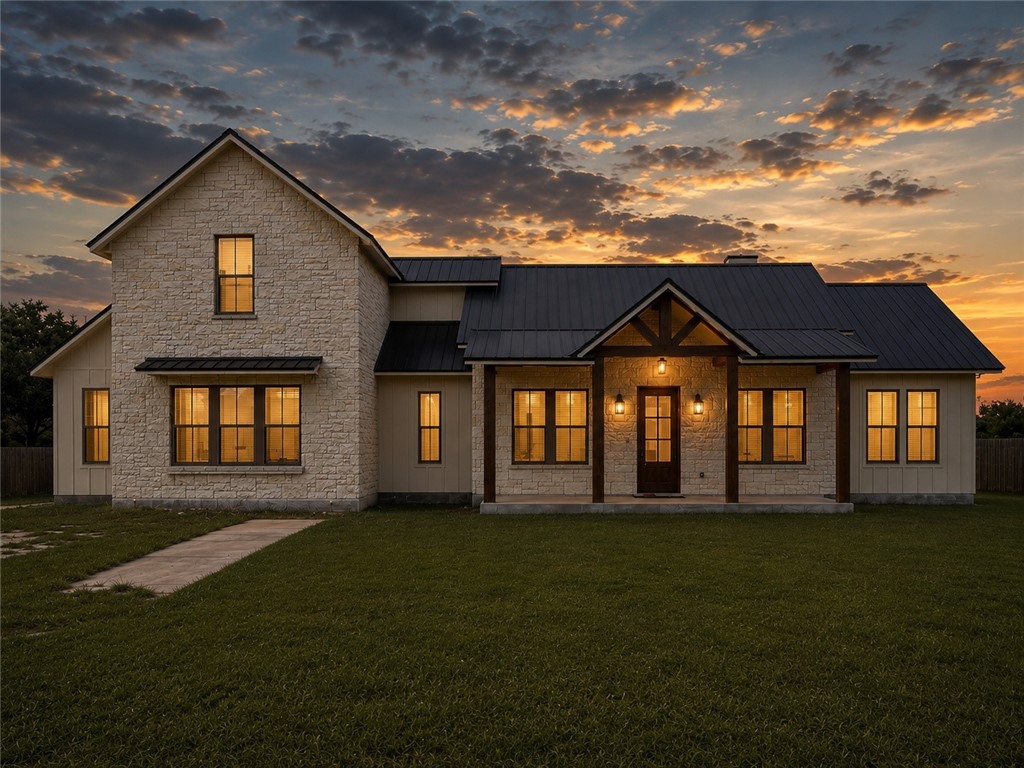 Stone-and-siding home with a dark metal roof and warmly lit windows at sunset.