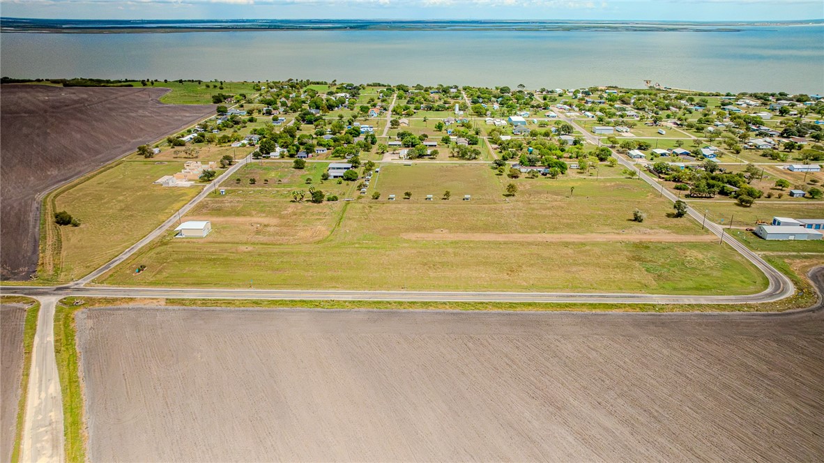Aerial view of vacant land beside a road, with fields, homes, and water in the distance.