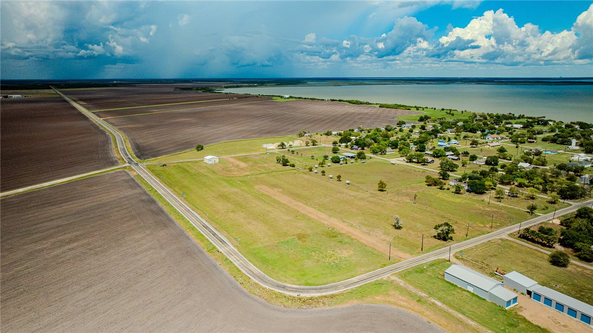 Aerial view of open rural land bordered by farmland, with scattered homes and water in the distance.