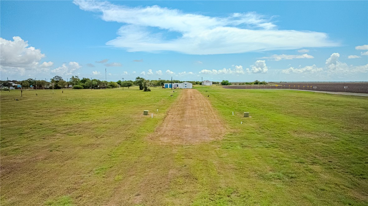 Grassy rural property with a dirt driveway leading to small outbuildings beside a cultivated field.