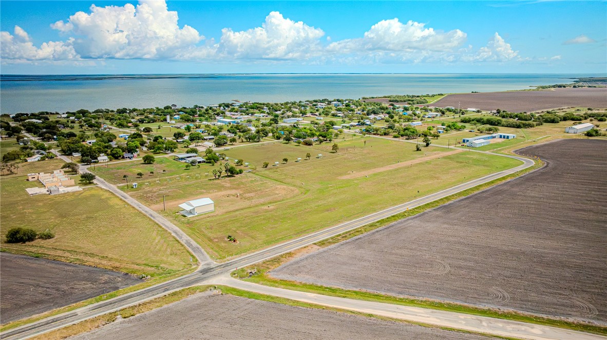Aerial view of a coastal community, open lots, surrounding farmland, and a broad bay.