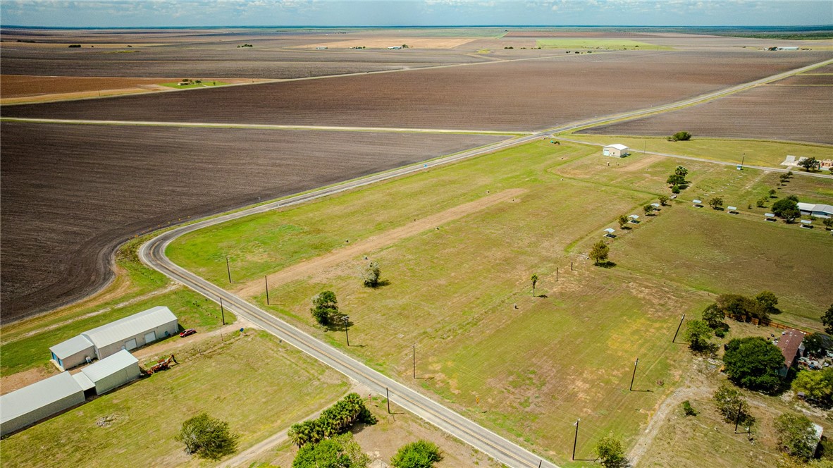 Aerial view of open rural land with outbuildings, a bordering road, and surrounding farm fields.