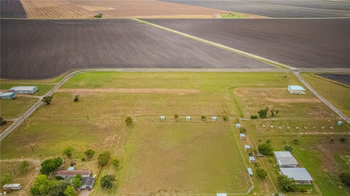 Aerial view of open rural land bordered by cultivated fields, with scattered trees and buildings.