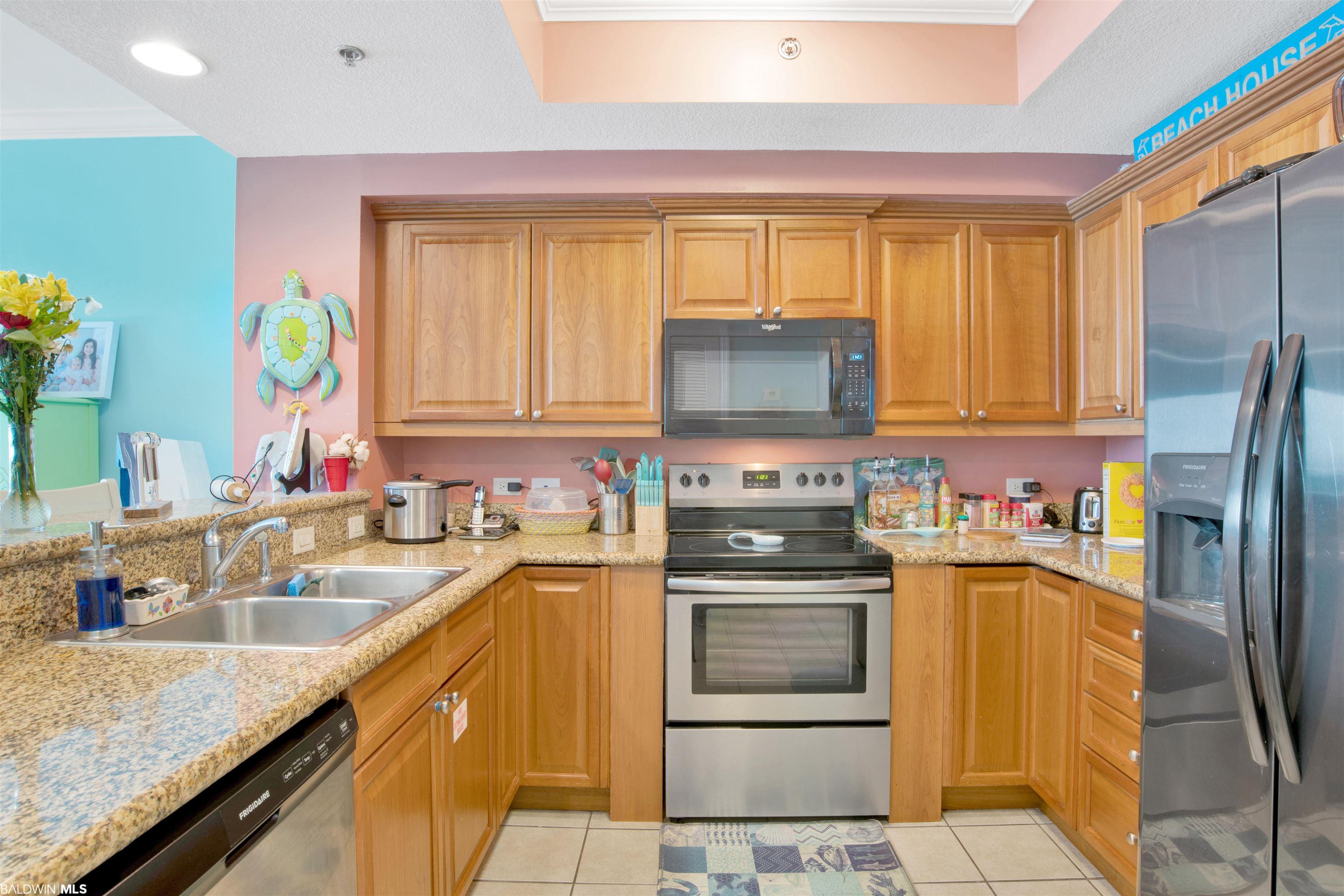 Condo kitchen with wood cabinets, granite counters, stainless appliances, and a colorful sea turtle clock.