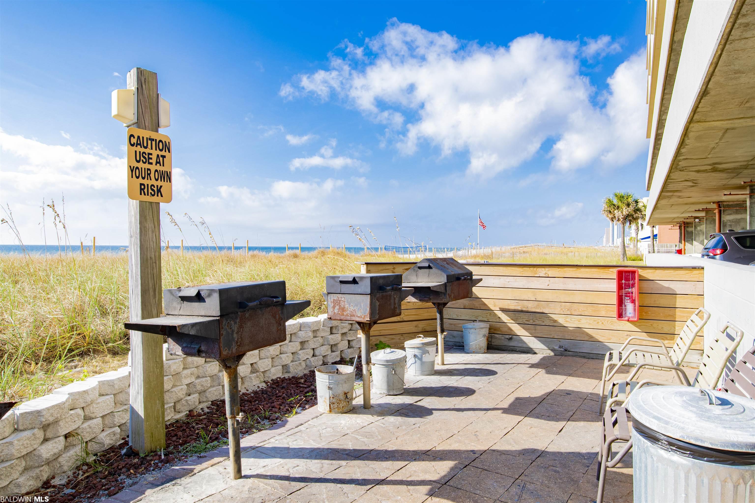 Beachfront patio with several grills and chairs overlooking dune grass and the Gulf shoreline.