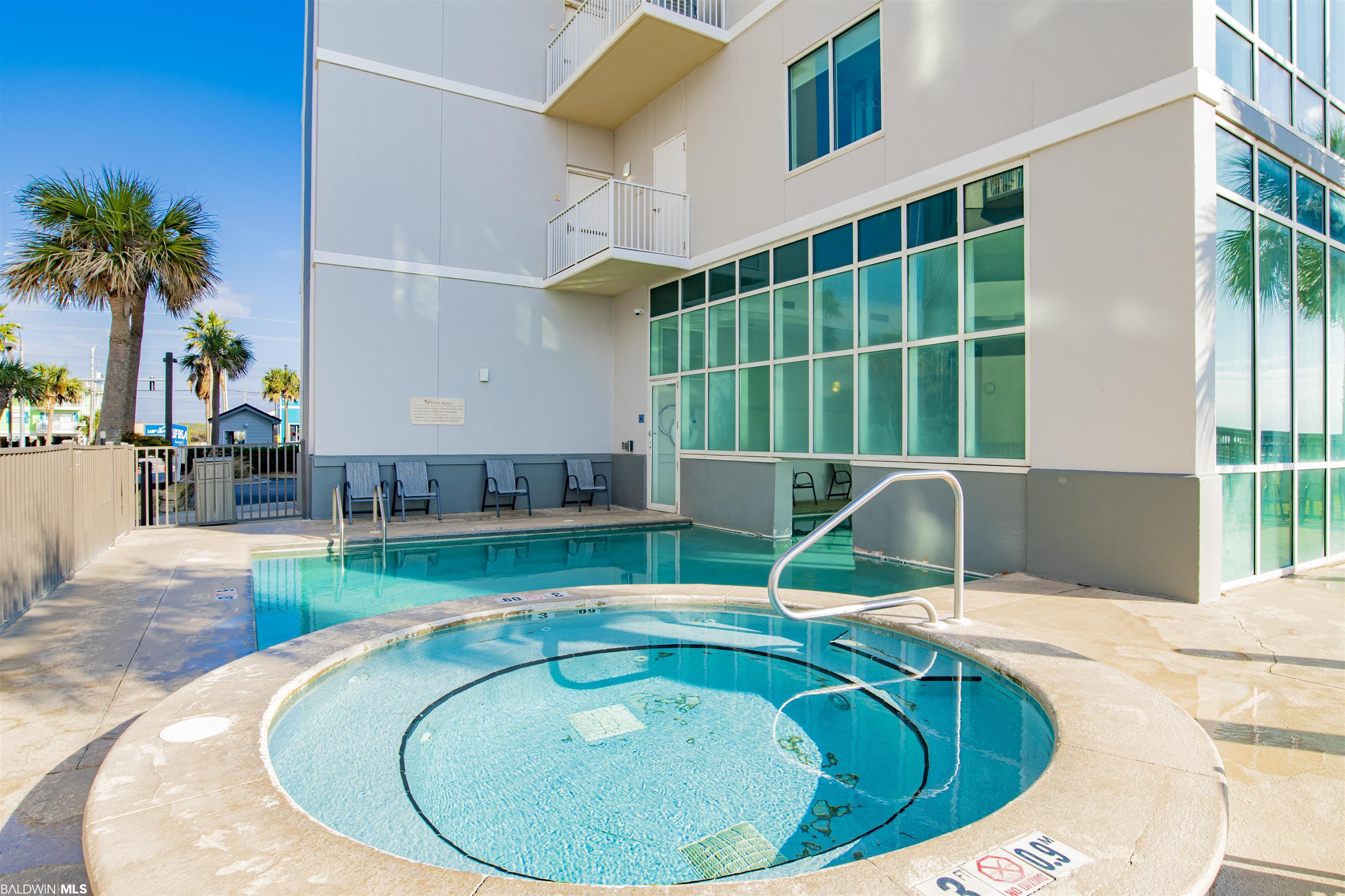 Outdoor pool and circular spa beside a modern condominium, with palm trees.