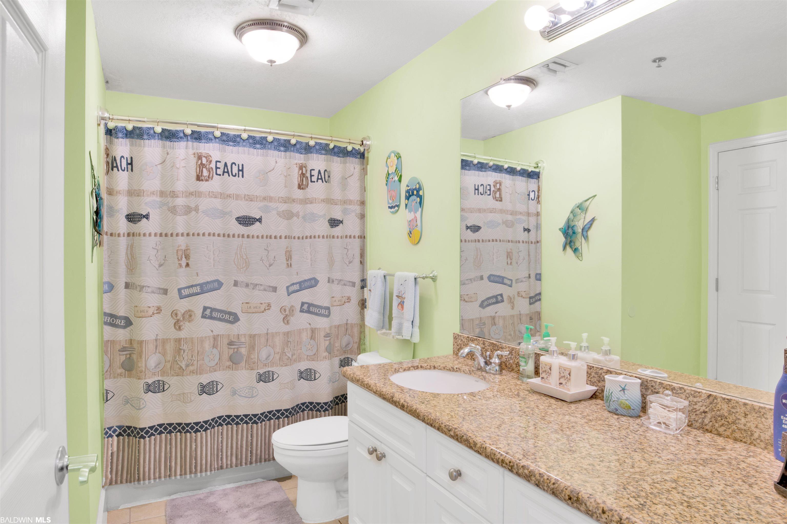 Bathroom with a beach-themed shower curtain and long granite vanity beneath a large mirror.