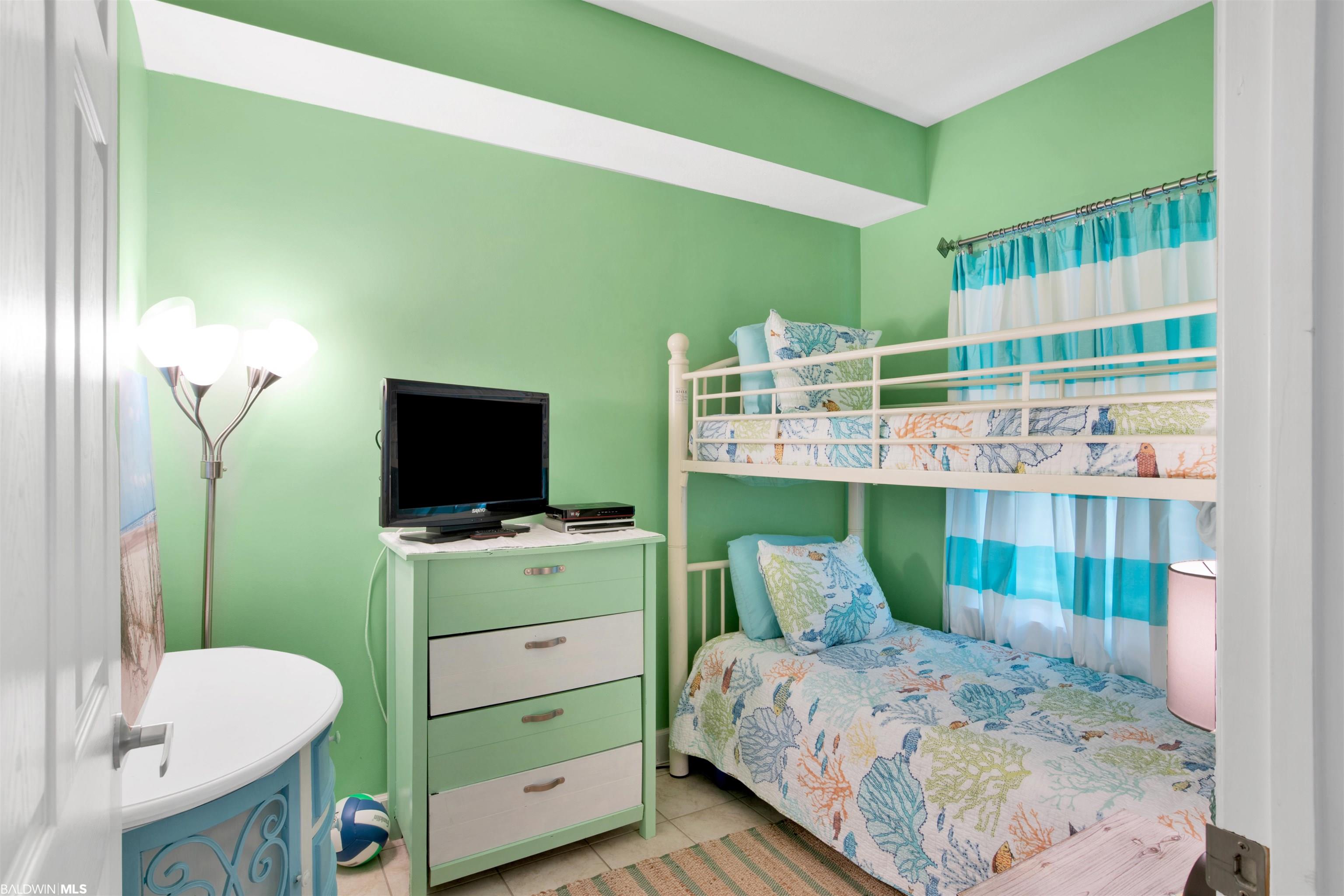 Bedroom with a white bunk bed, coastal-patterned bedding, mint-green walls, and turquoise curtains.