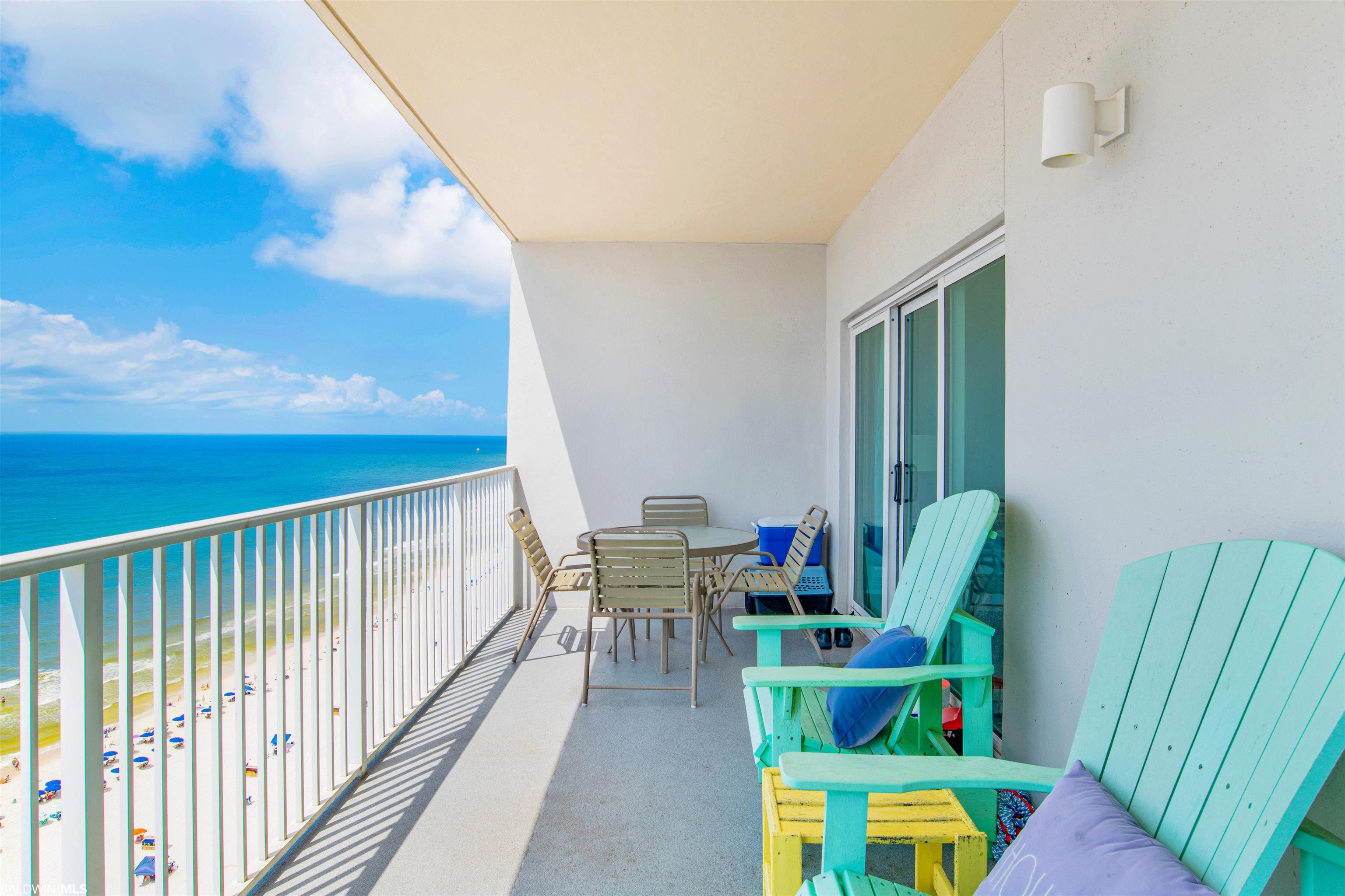 Condo balcony with turquoise chairs and a dining table overlooking the Gulf and beach.