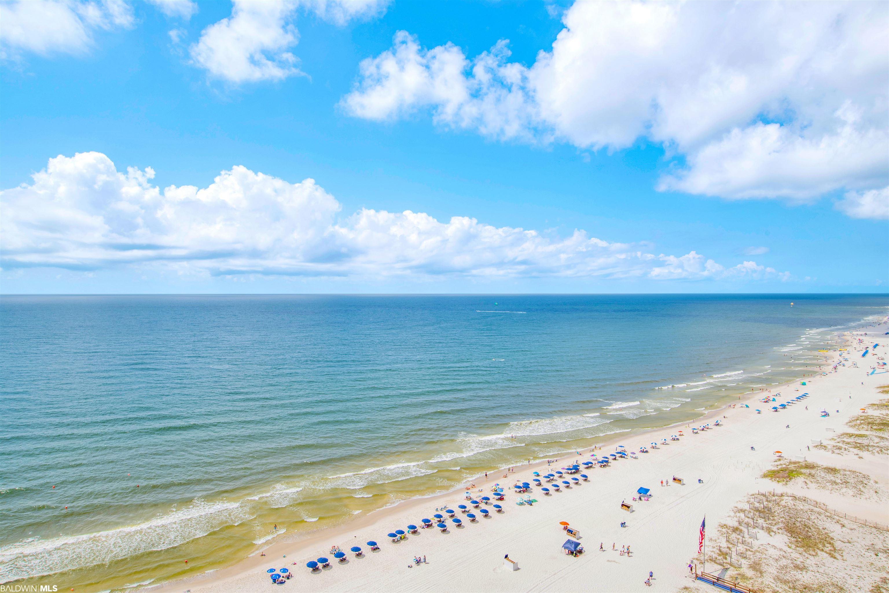 Panoramic beach view with gentle waves, white sand, and rows of colorful umbrellas.