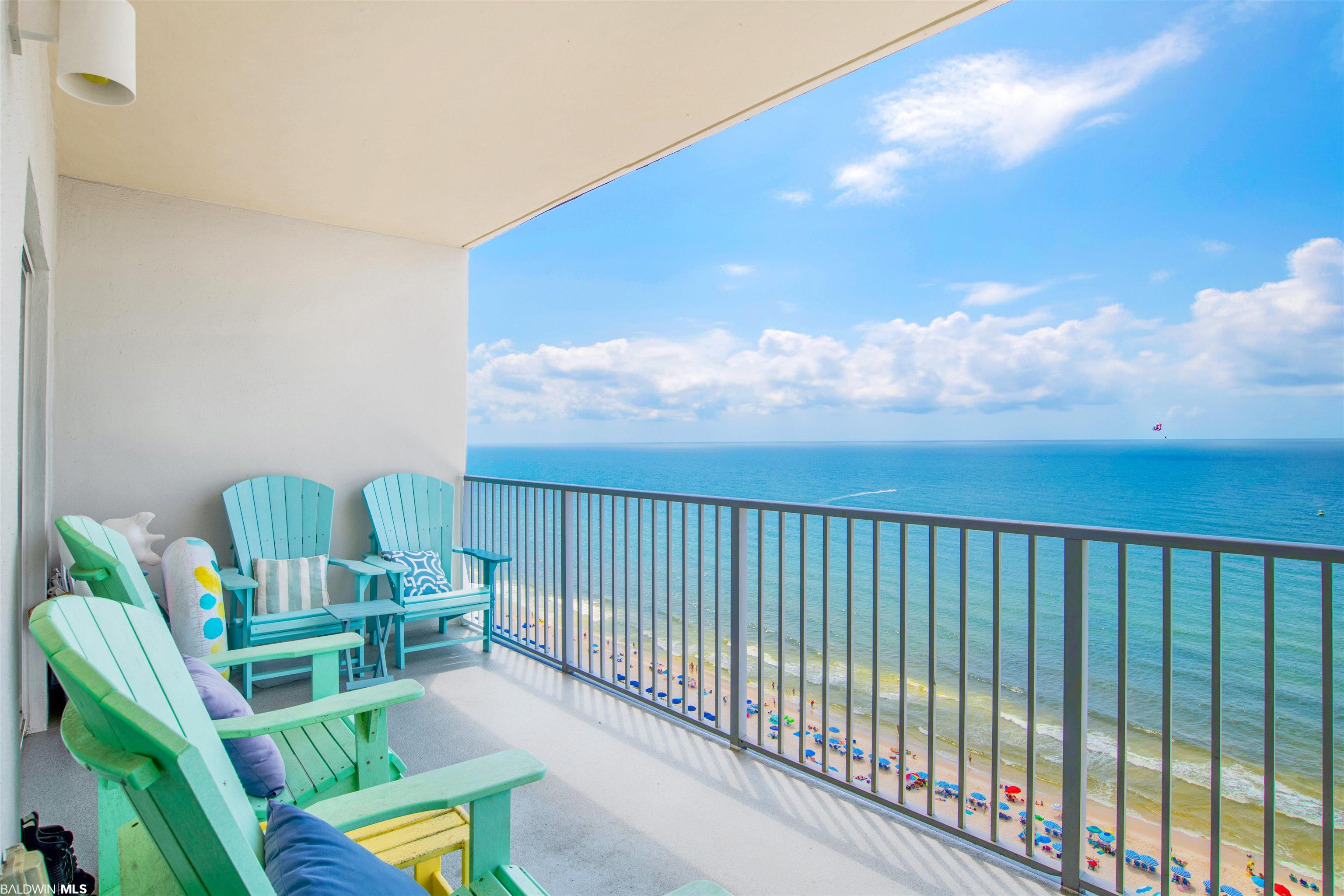 Condo balcony with colorful chairs overlooking the Gulf and a crowded sandy beach.