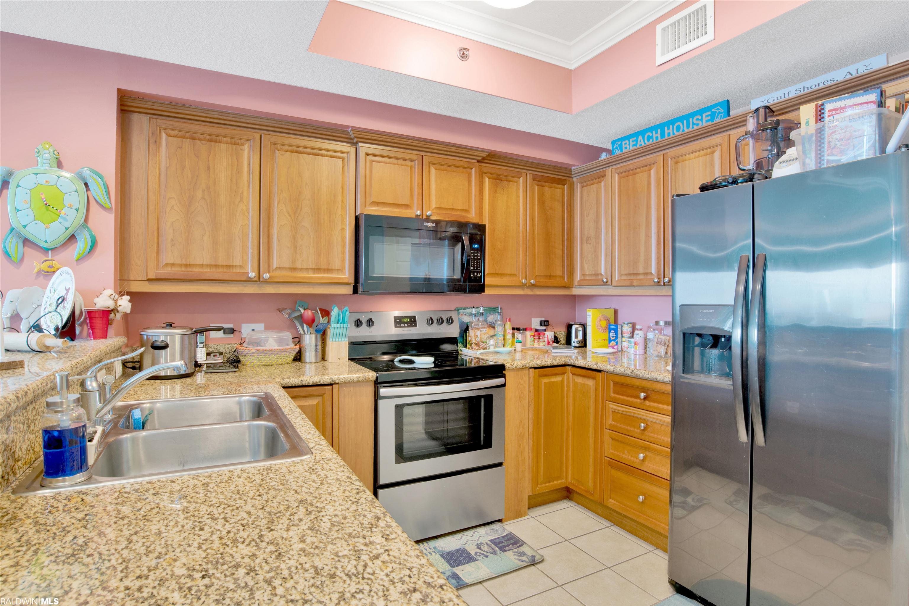 Condo kitchen with honey-colored cabinets, granite counters, stainless steel appliances, and coastal turtle decor.