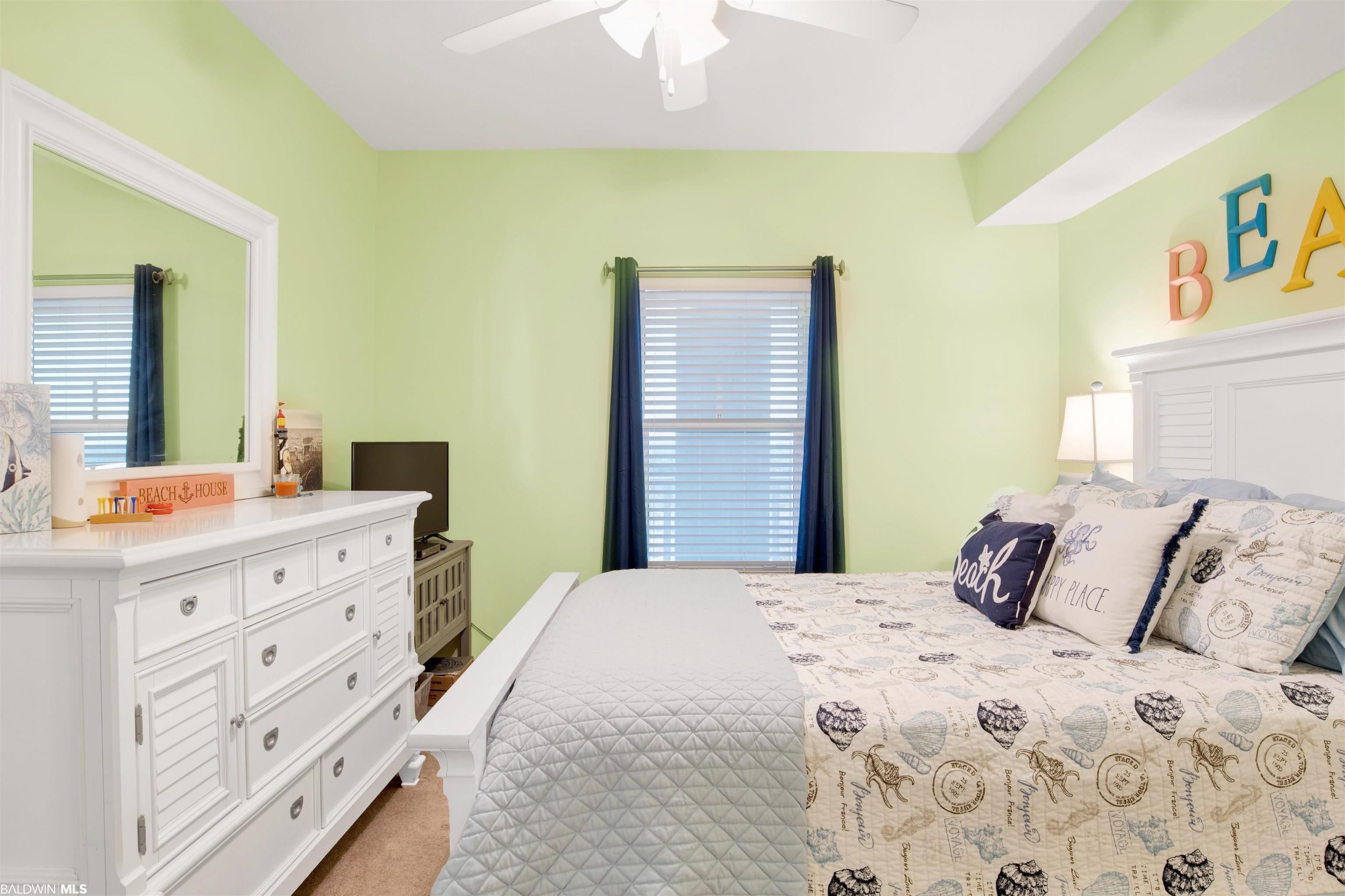 Bedroom with pale green walls, coastal-print bedding, navy curtains, and a white dresser.