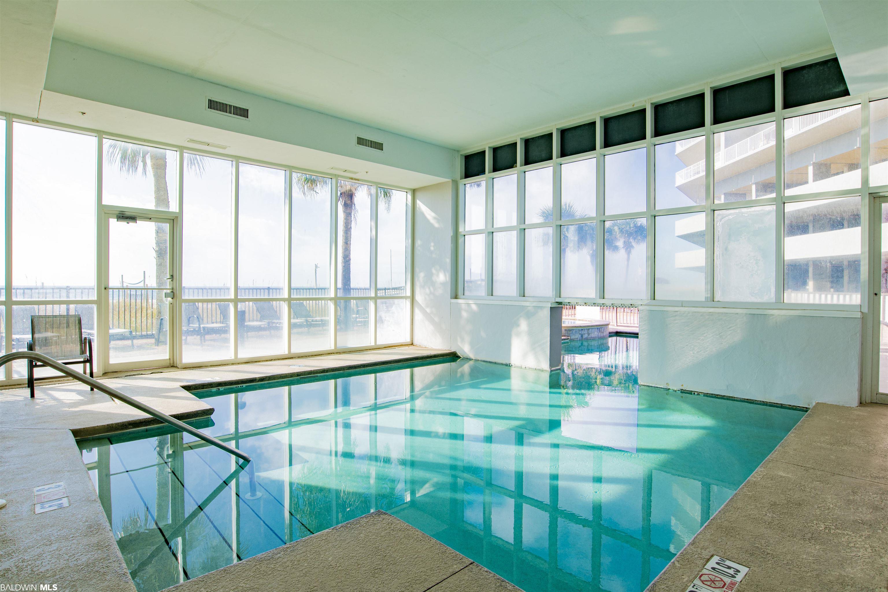 Indoor swimming pool beneath tall windows, with palm trees visible outside.
