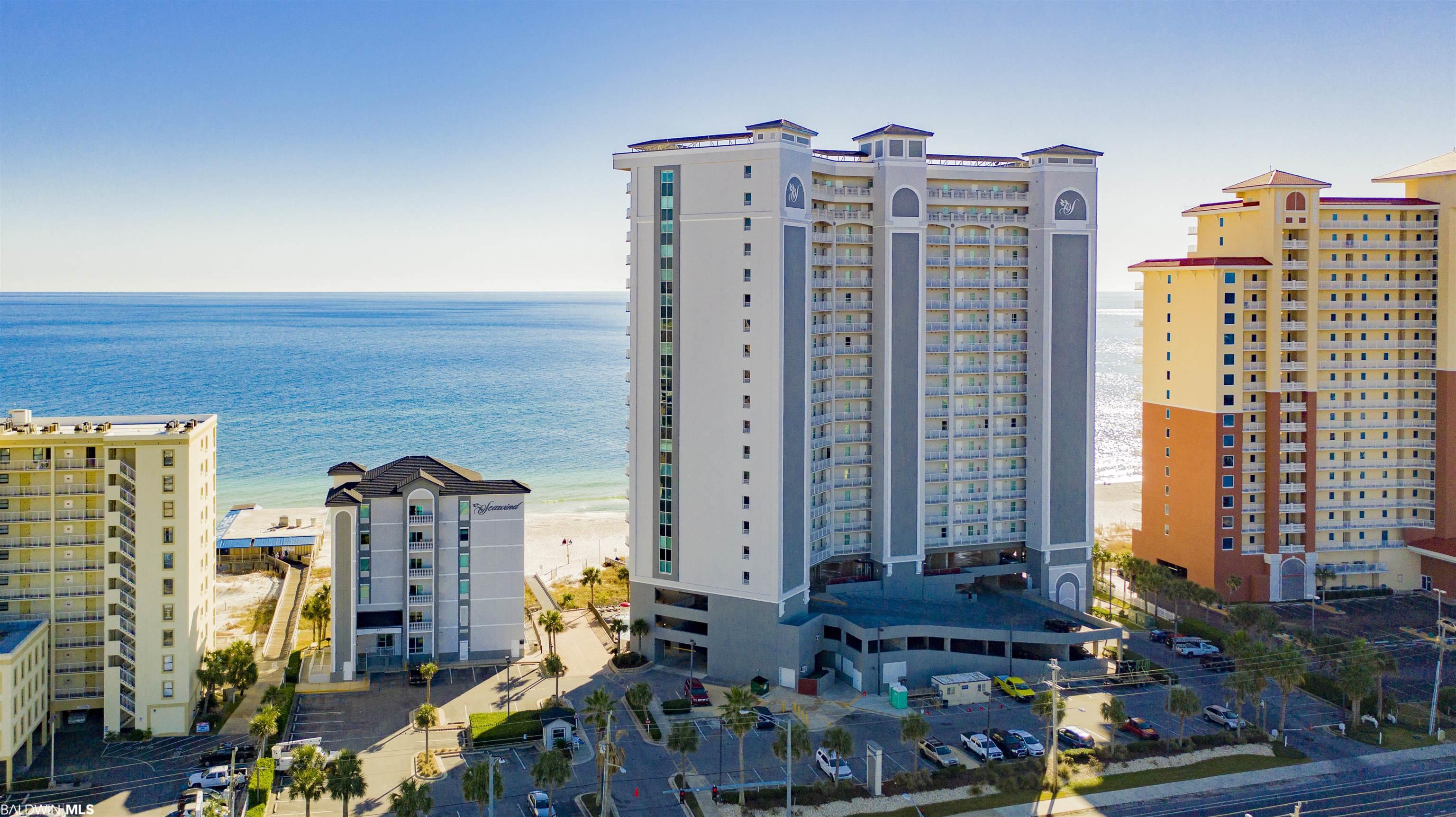 Beachfront condominium tower beside the Gulf, seen with neighboring buildings and the shoreline.