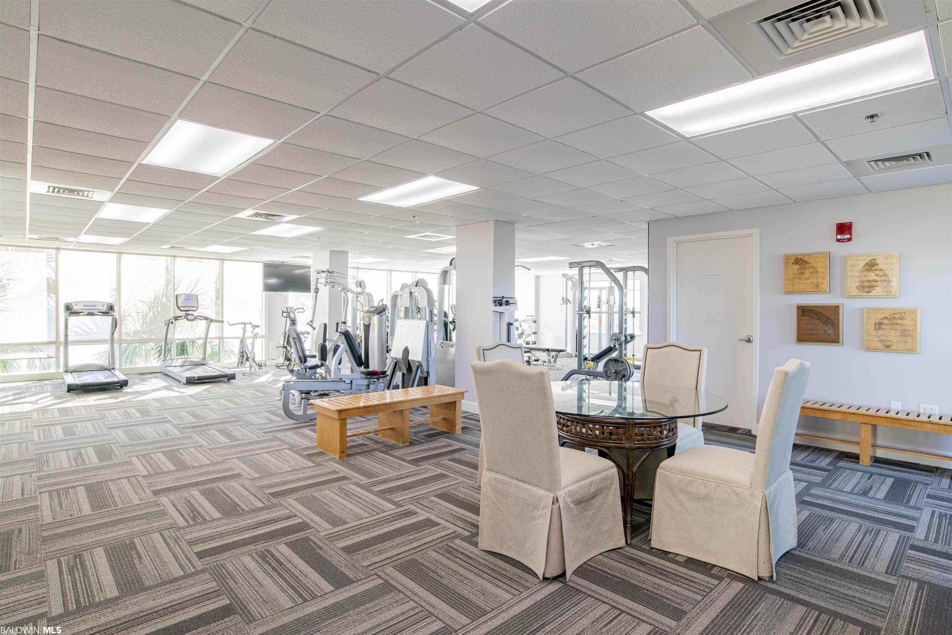 Fitness room with treadmills, weight machines, and a glass table with upholstered chairs.