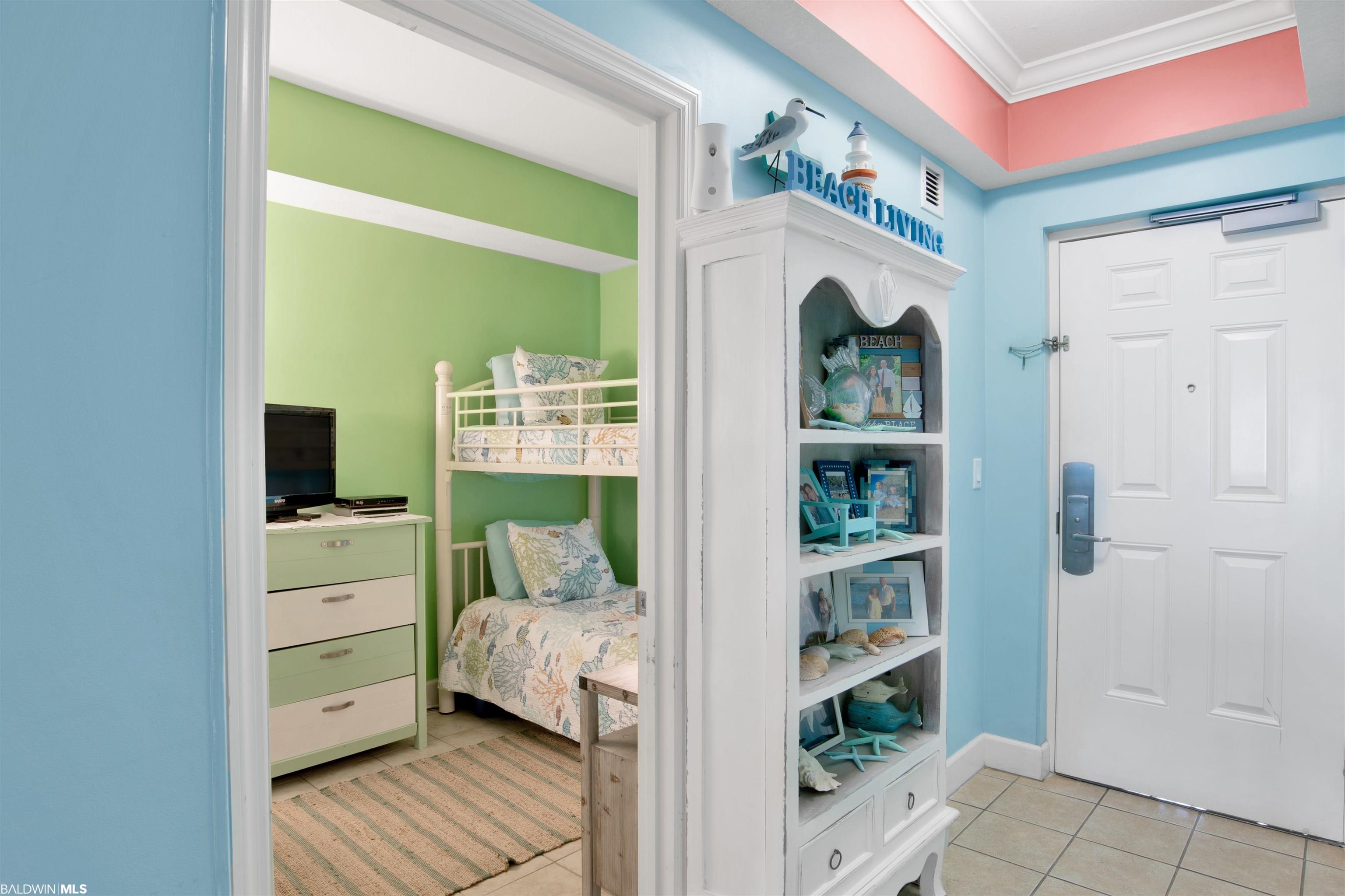 Condo entryway beside a green bedroom with a white bunk bed and beach-themed display cabinet.
