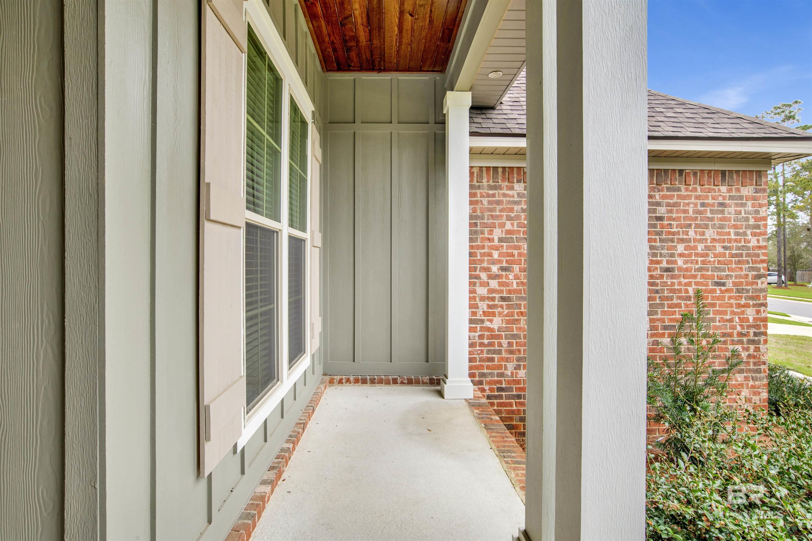 Covered front porch with a wood-plank ceiling, white columns, and brick accents.