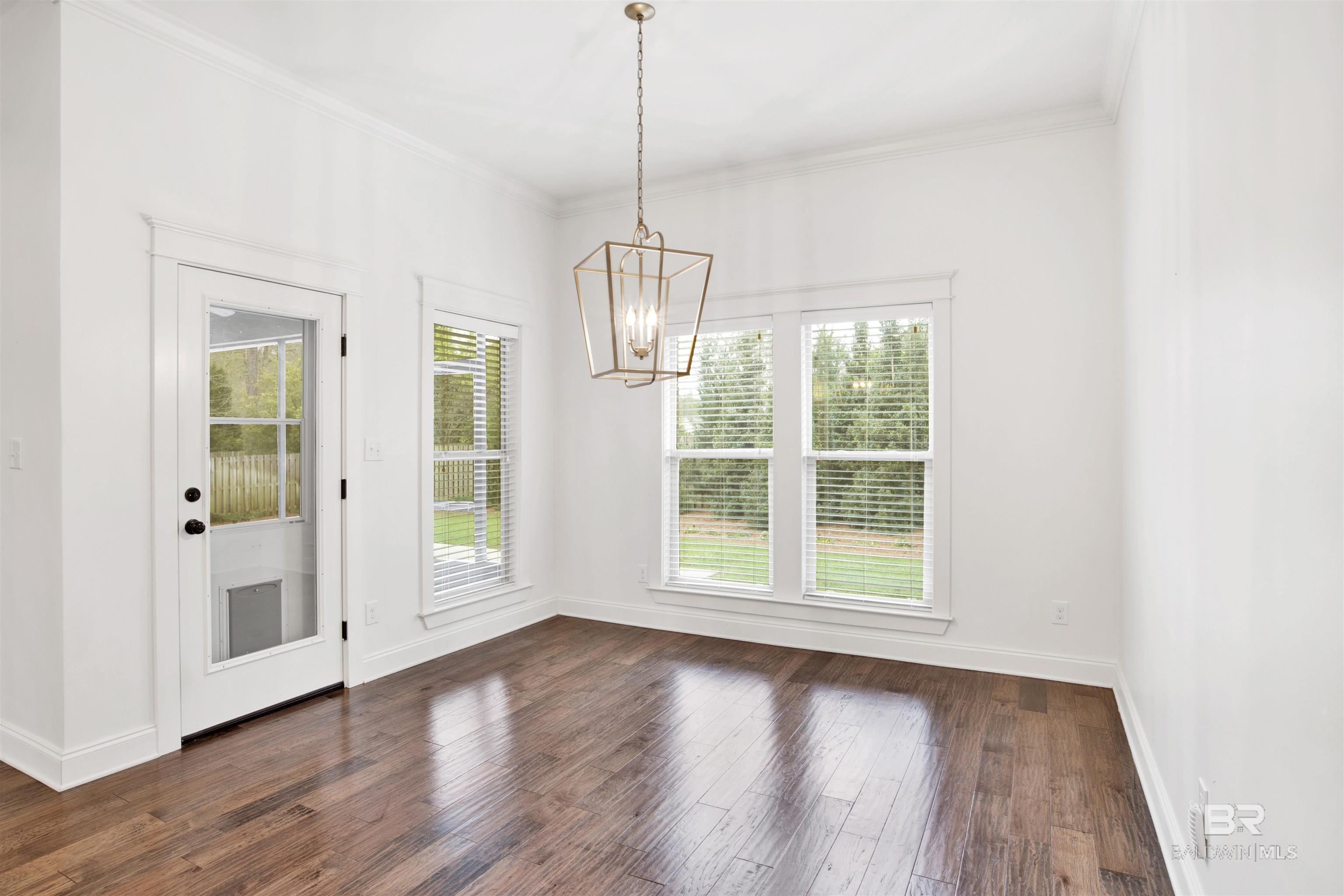 Unfurnished dining room with dark hardwood floors, a geometric chandelier, and windows overlooking greenery.