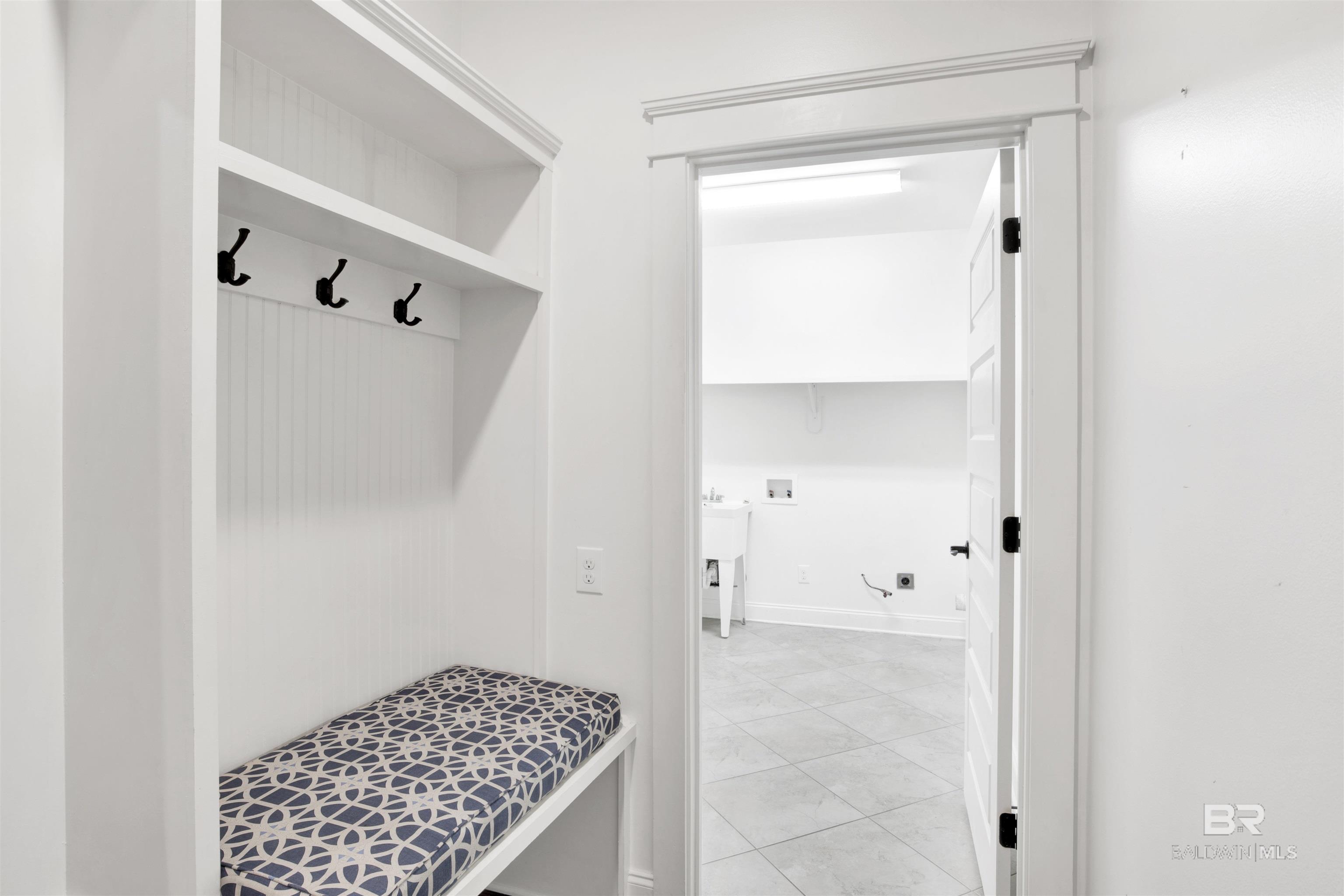 Mudroom bench with patterned cushion and coat hooks beside a tiled laundry room.