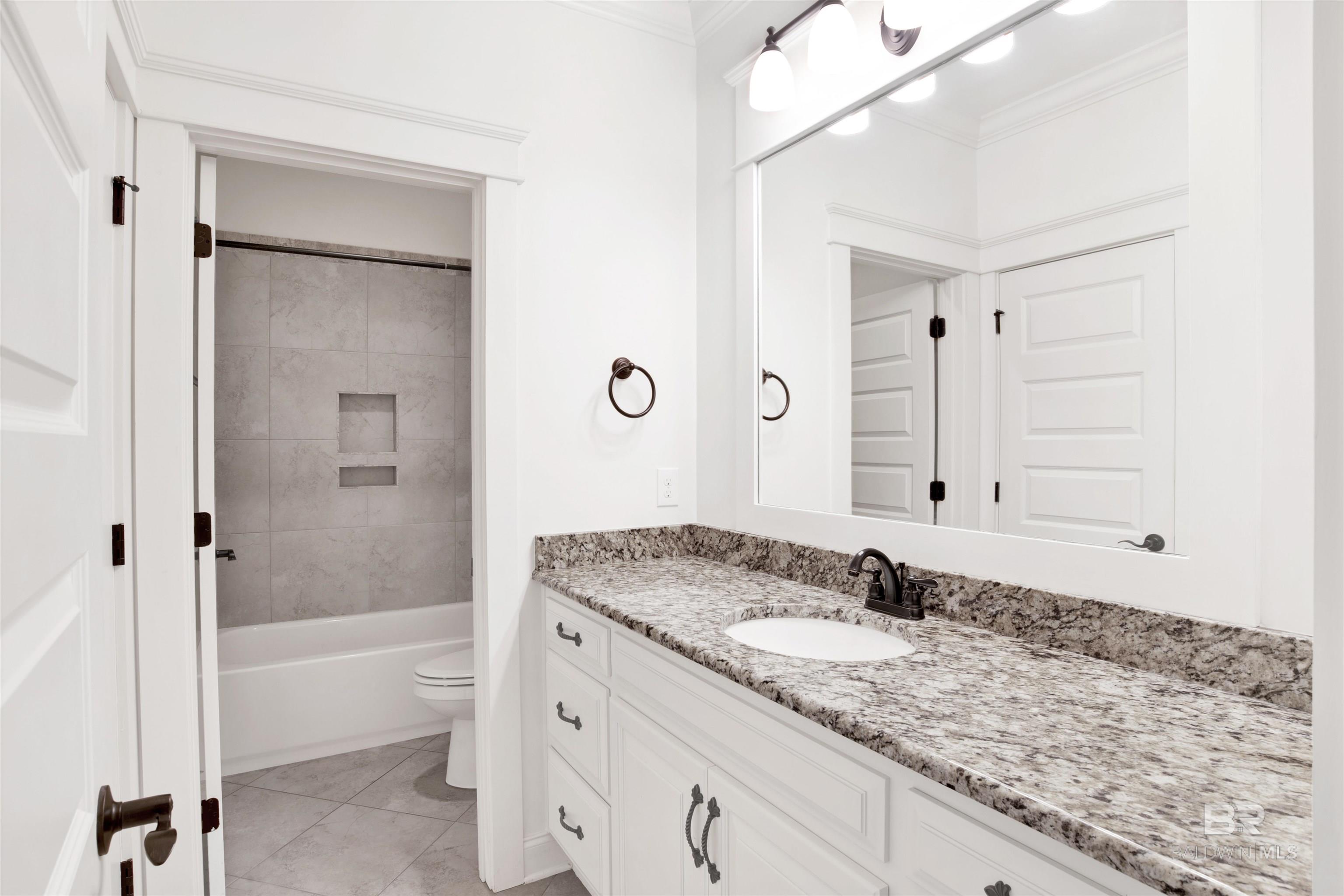 Bathroom with a granite-topped vanity and tiled tub-shower alcove with recessed niches.