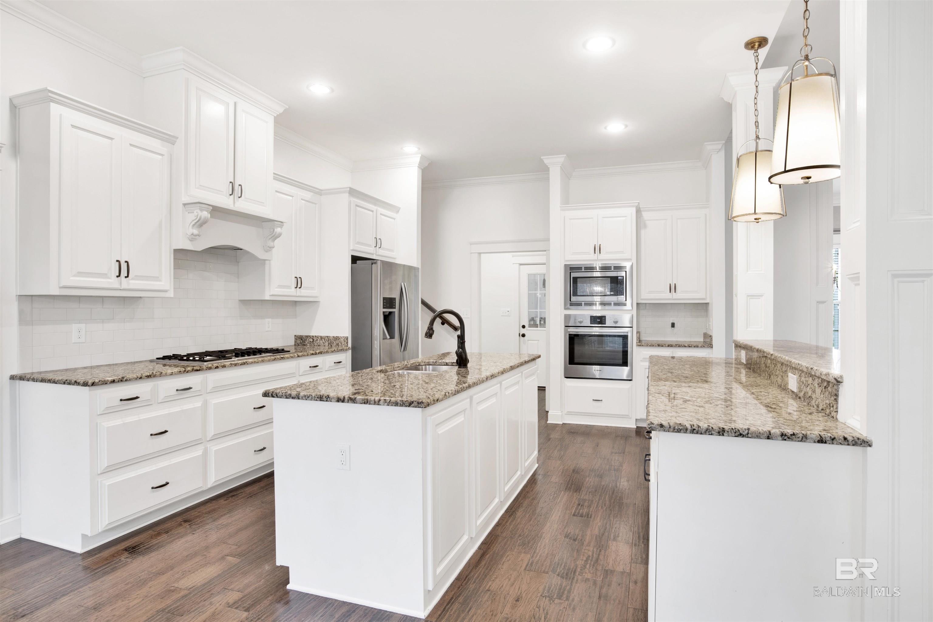 Bright white kitchen with granite counters, a central island, and stainless steel appliances.