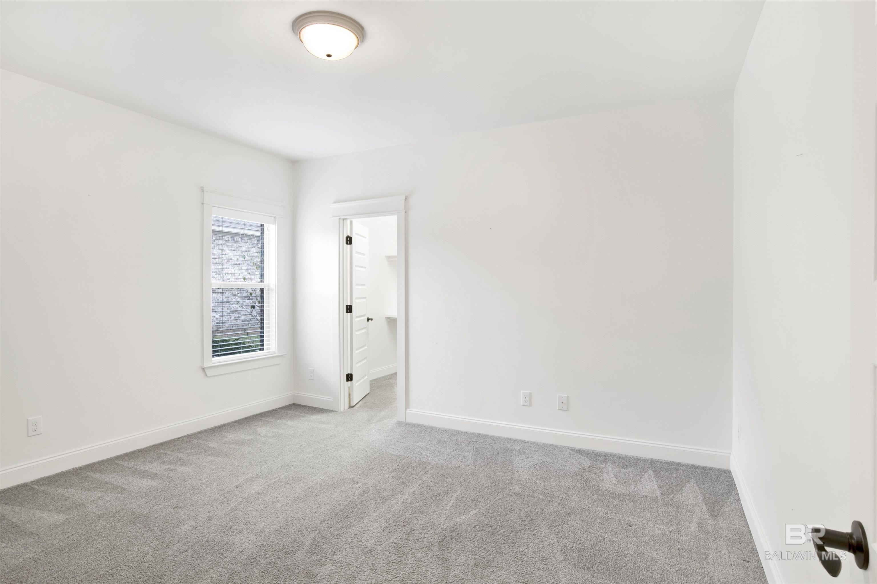 Empty bedroom with gray carpet, white walls, and a window beside an open doorway.