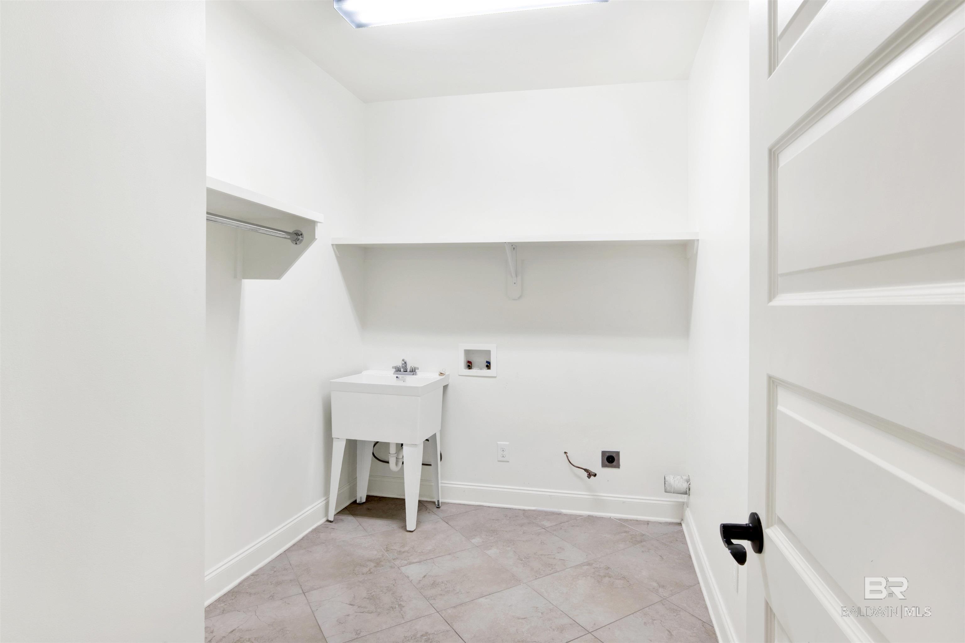 Laundry room with tiled floor, utility sink, washer and dryer hookups, and a high shelf.