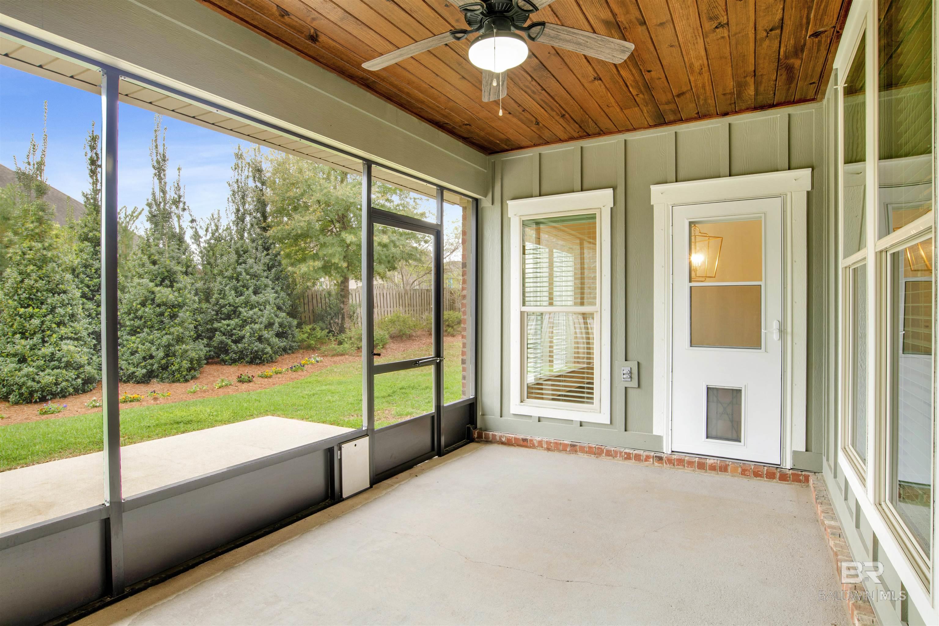 Screened-in porch with a wood-plank ceiling, ceiling fan, and views of the landscaped yard.
