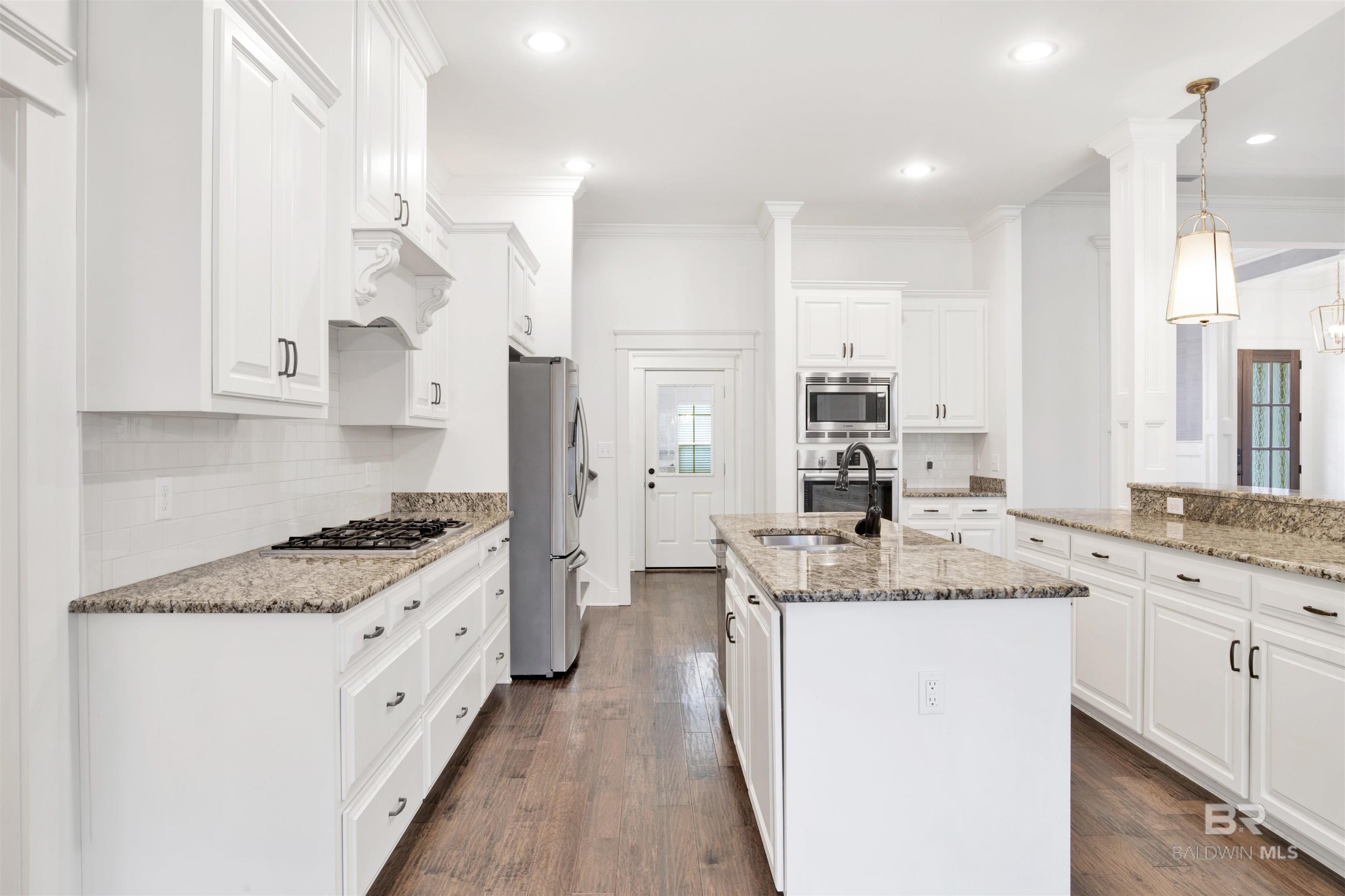 Bright kitchen with white cabinets, granite counters, a large sink island, and stainless steel appliances.