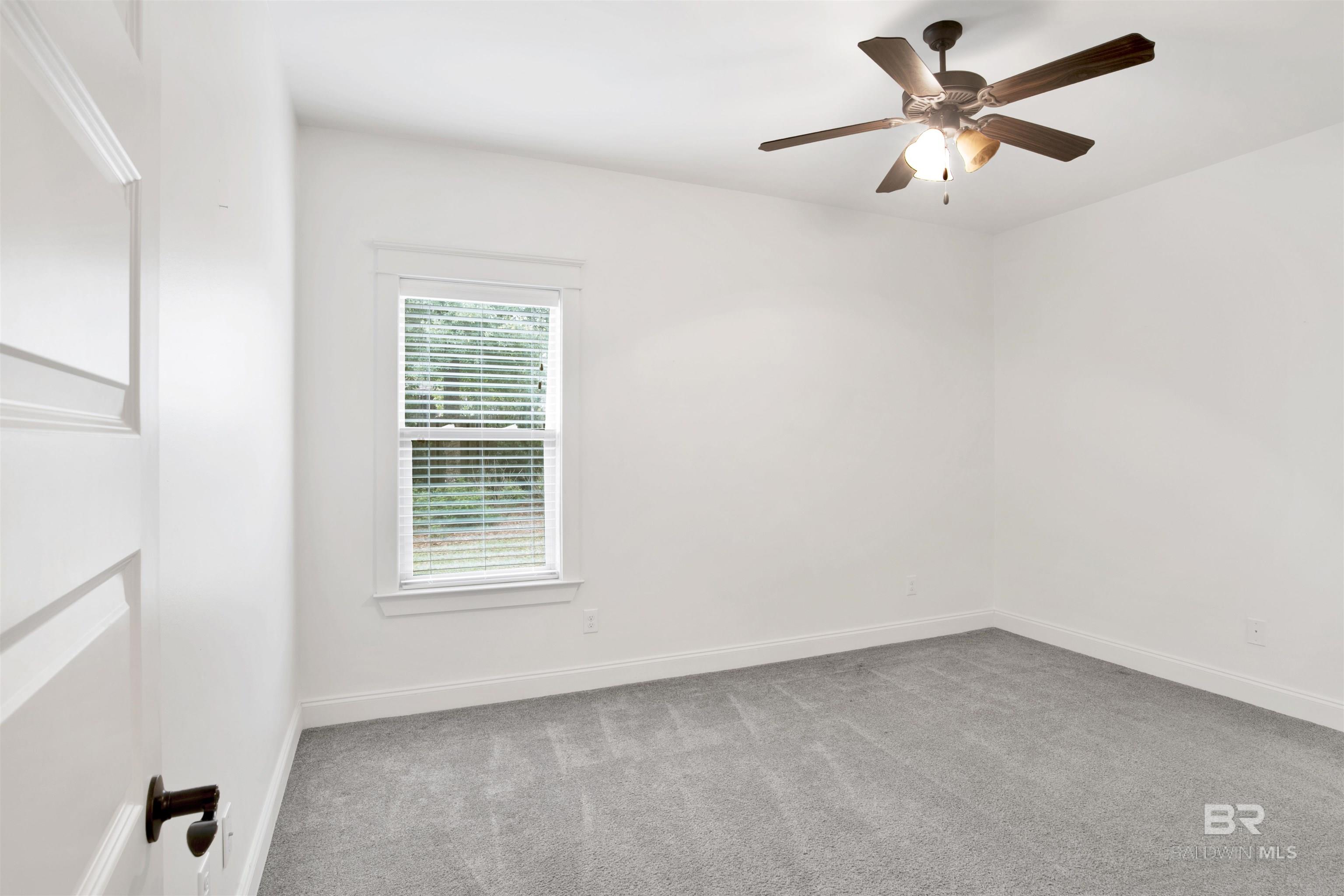 Empty bedroom with gray carpet, a window with blinds, and a dark wood ceiling fan.