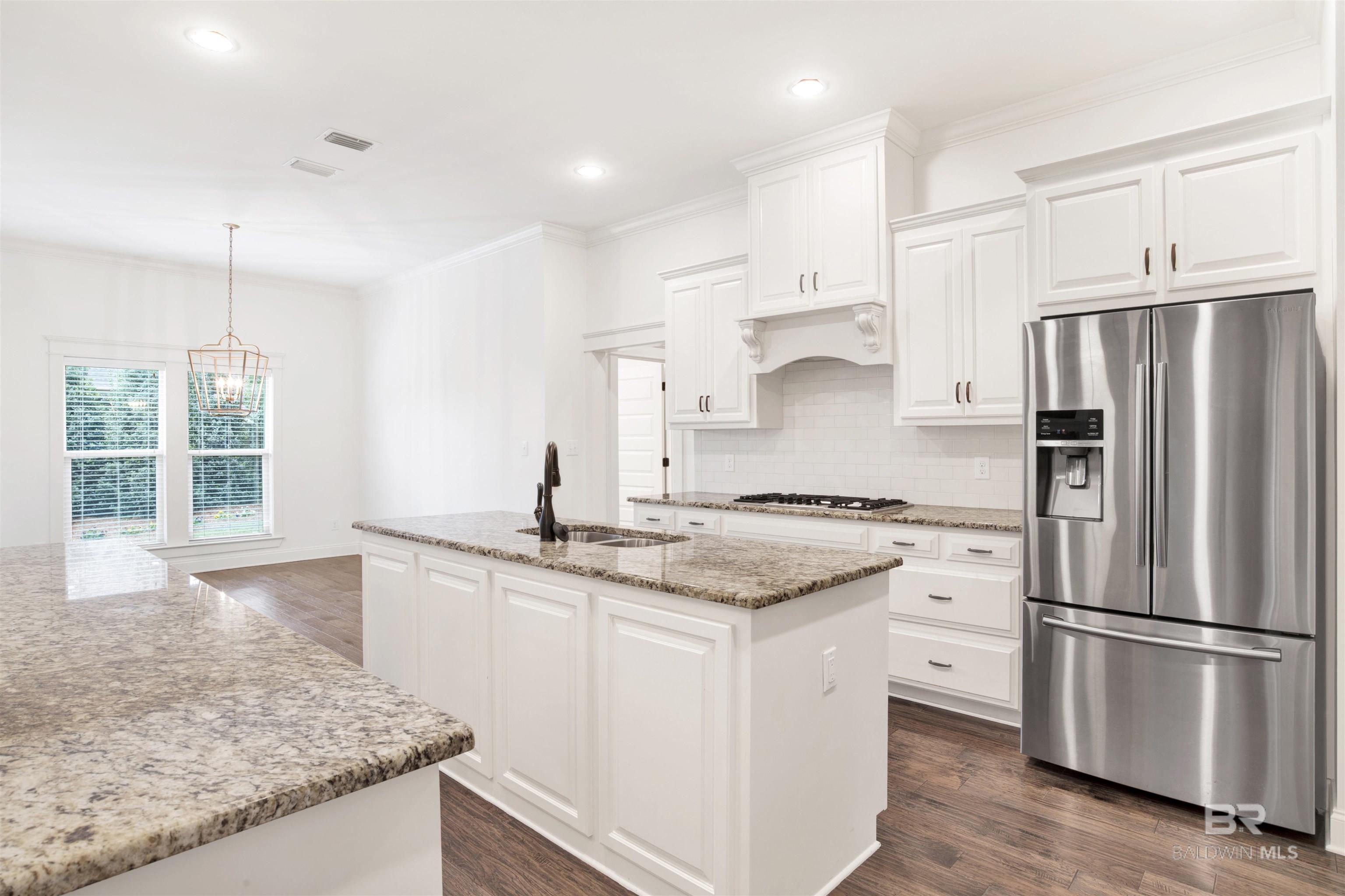 Bright kitchen with white cabinets, granite island, stainless steel refrigerator, and a window-side dining nook.