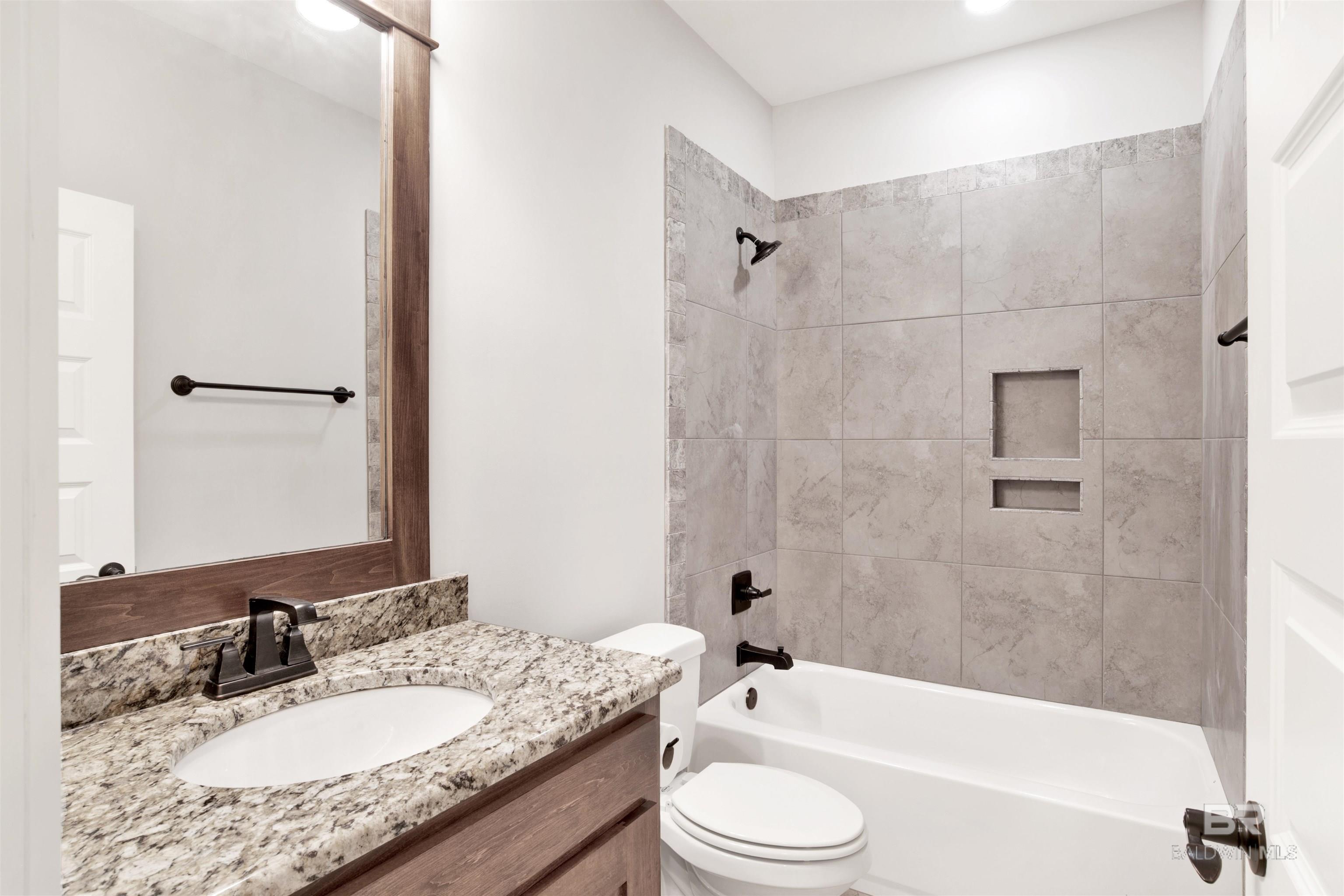 Bathroom with a granite vanity and wood-framed mirror beside a tiled tub and shower.