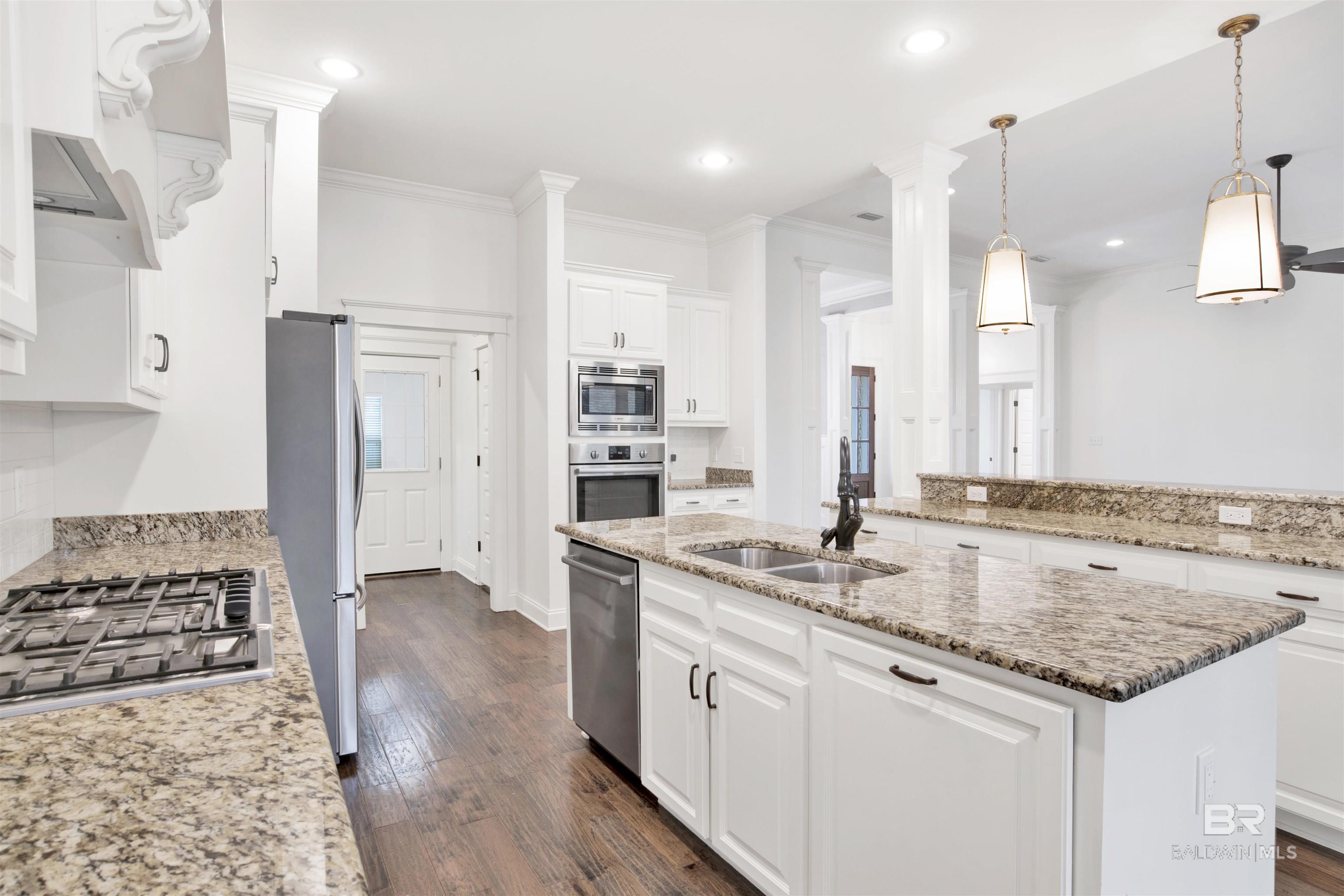 Bright white kitchen with granite island, double sink, stainless steel appliances, and wood-look flooring.