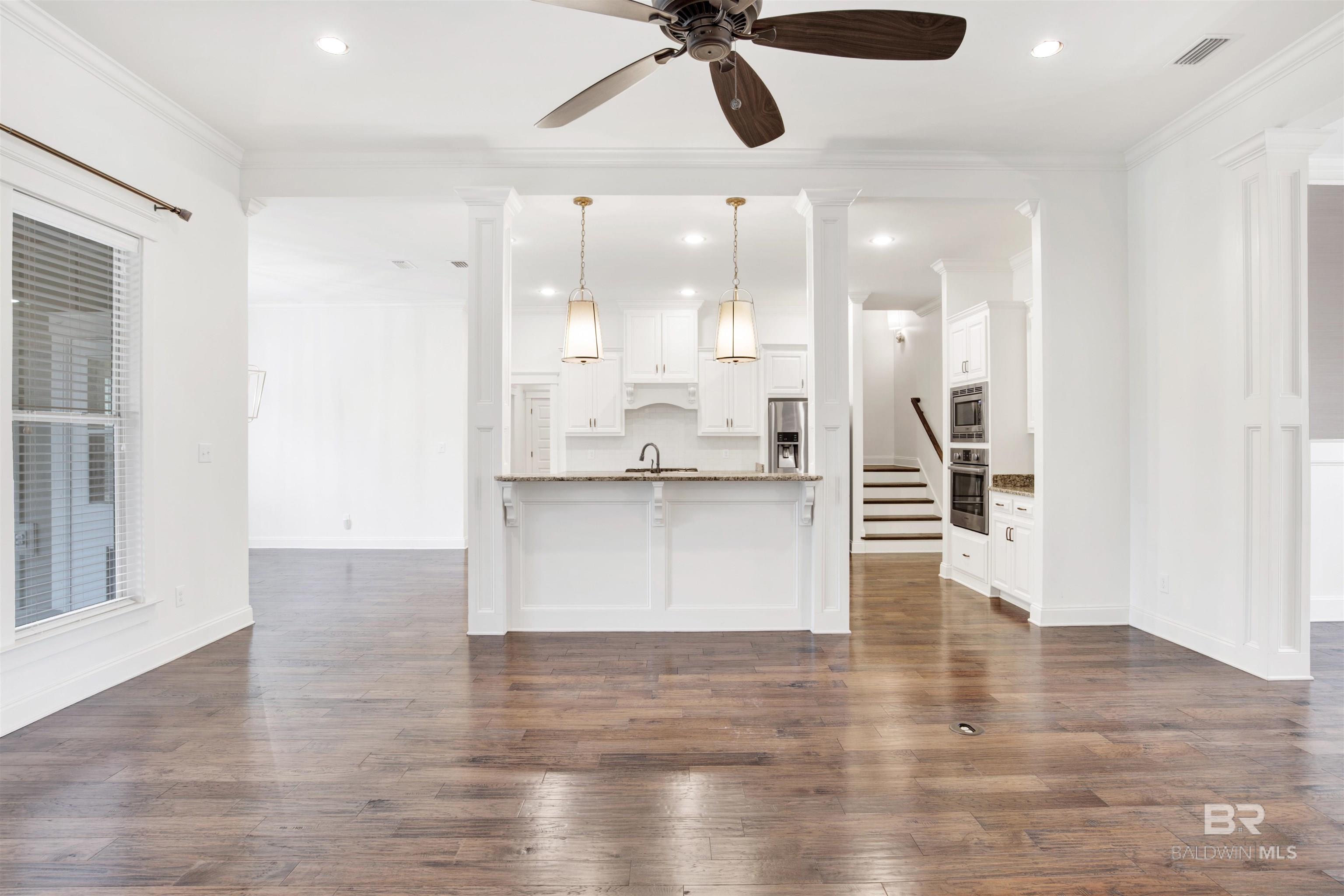 Open-plan kitchen with a granite island, white cabinetry, pendant lights, and wide-plank wood flooring.