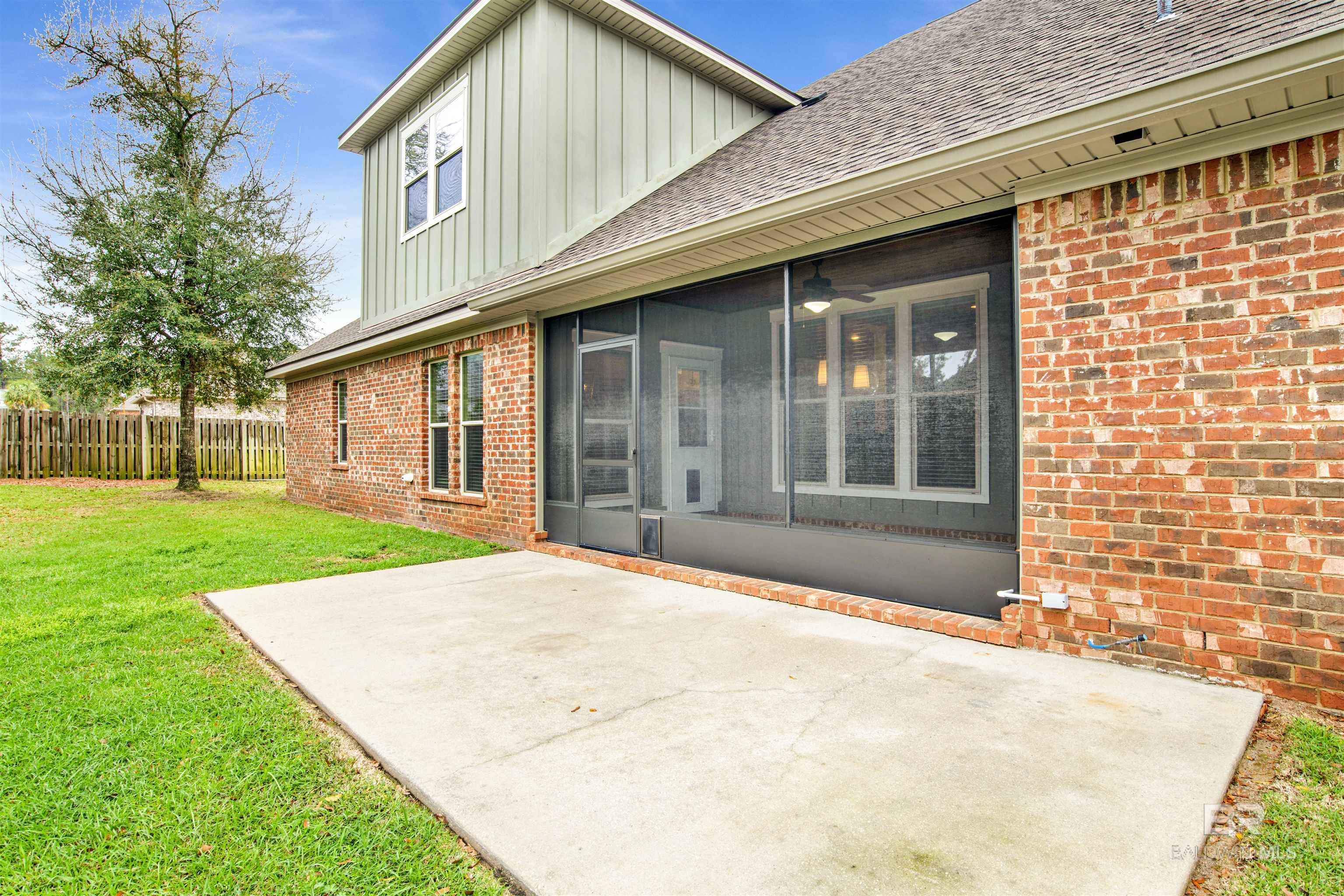 Brick home with a screened porch overlooking a broad concrete patio and fenced lawn.