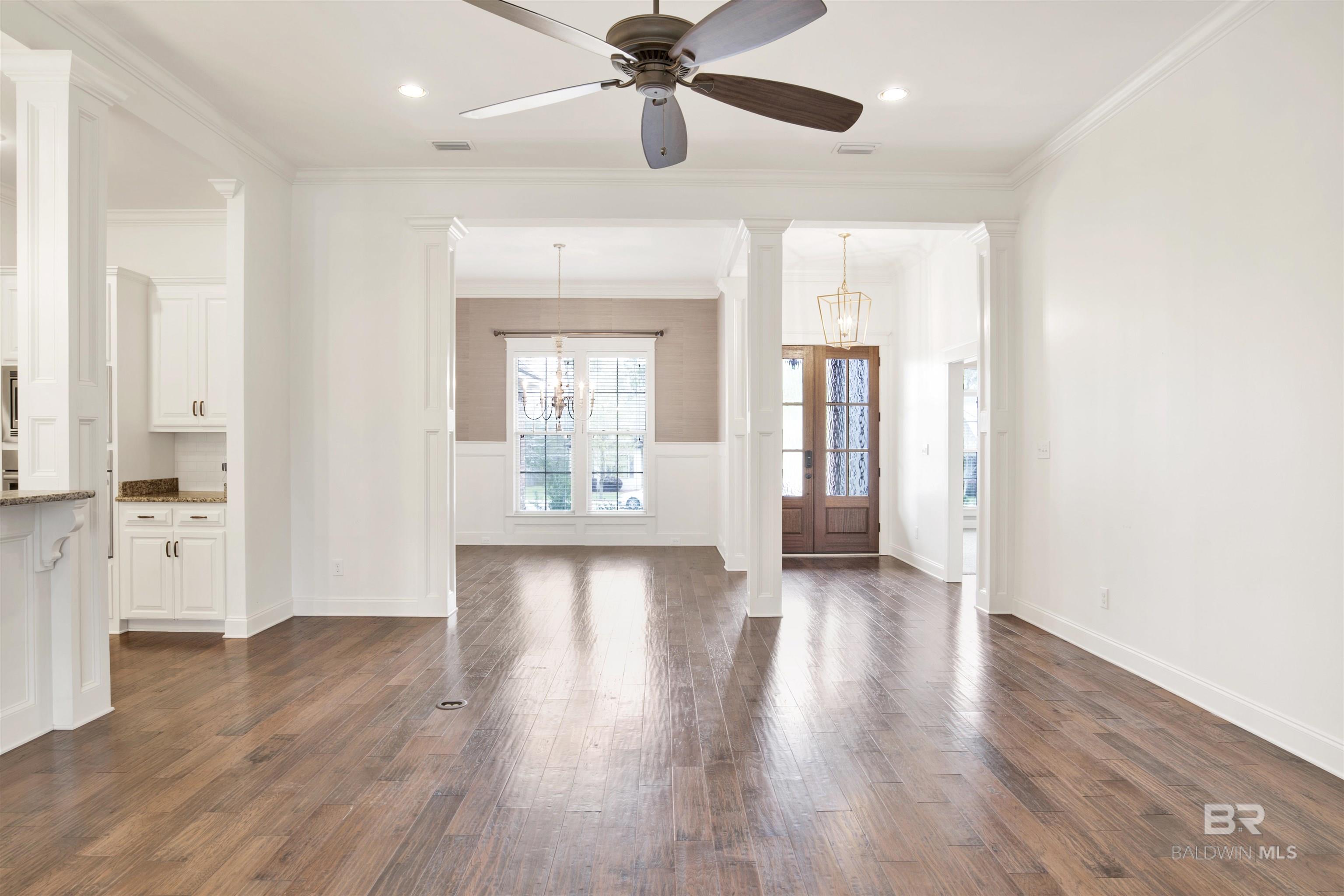 Vacant dining room with glossy hardwood floors, large windows, and a chandelier.