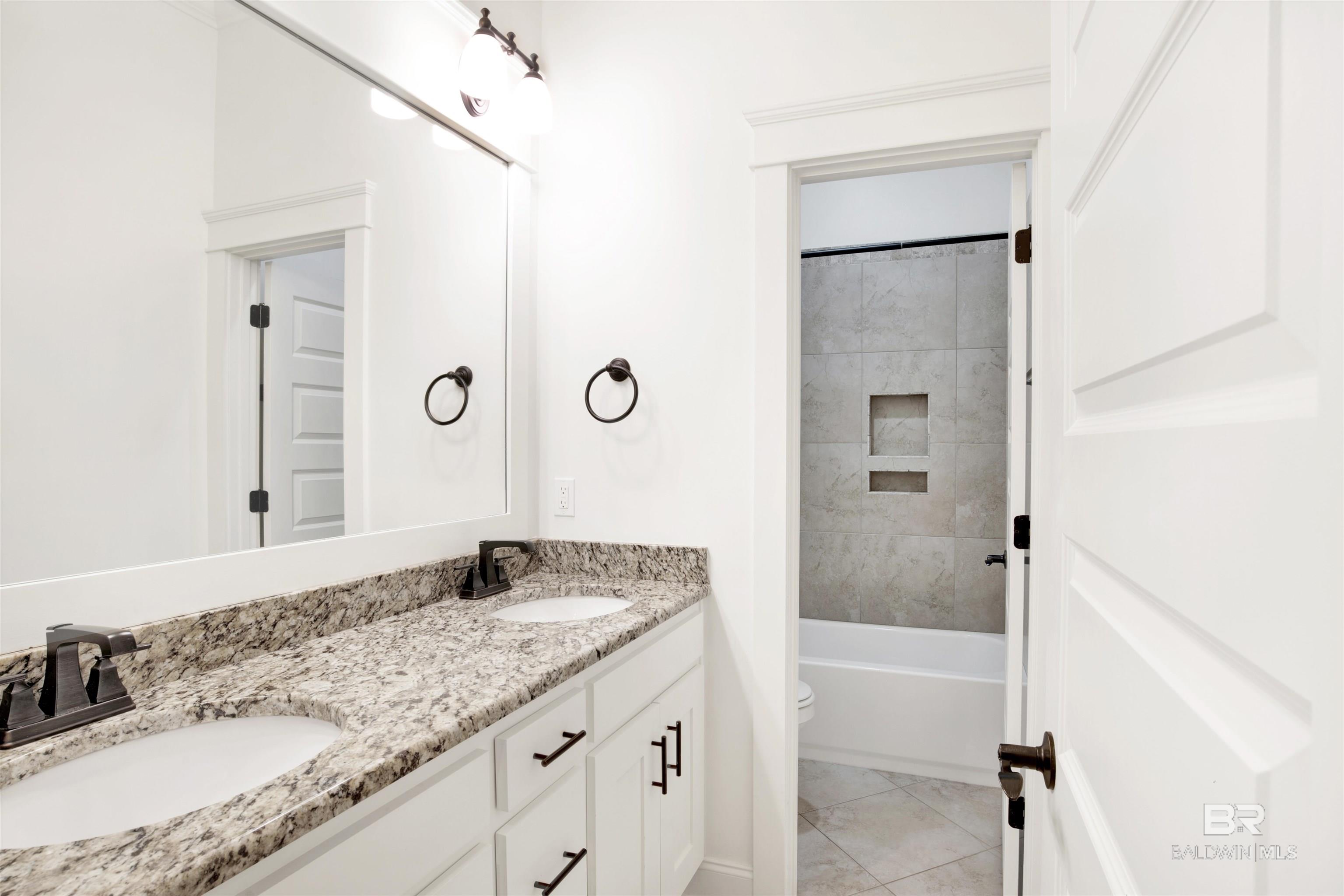 Bathroom with a double-sink stone vanity and tiled tub and shower.