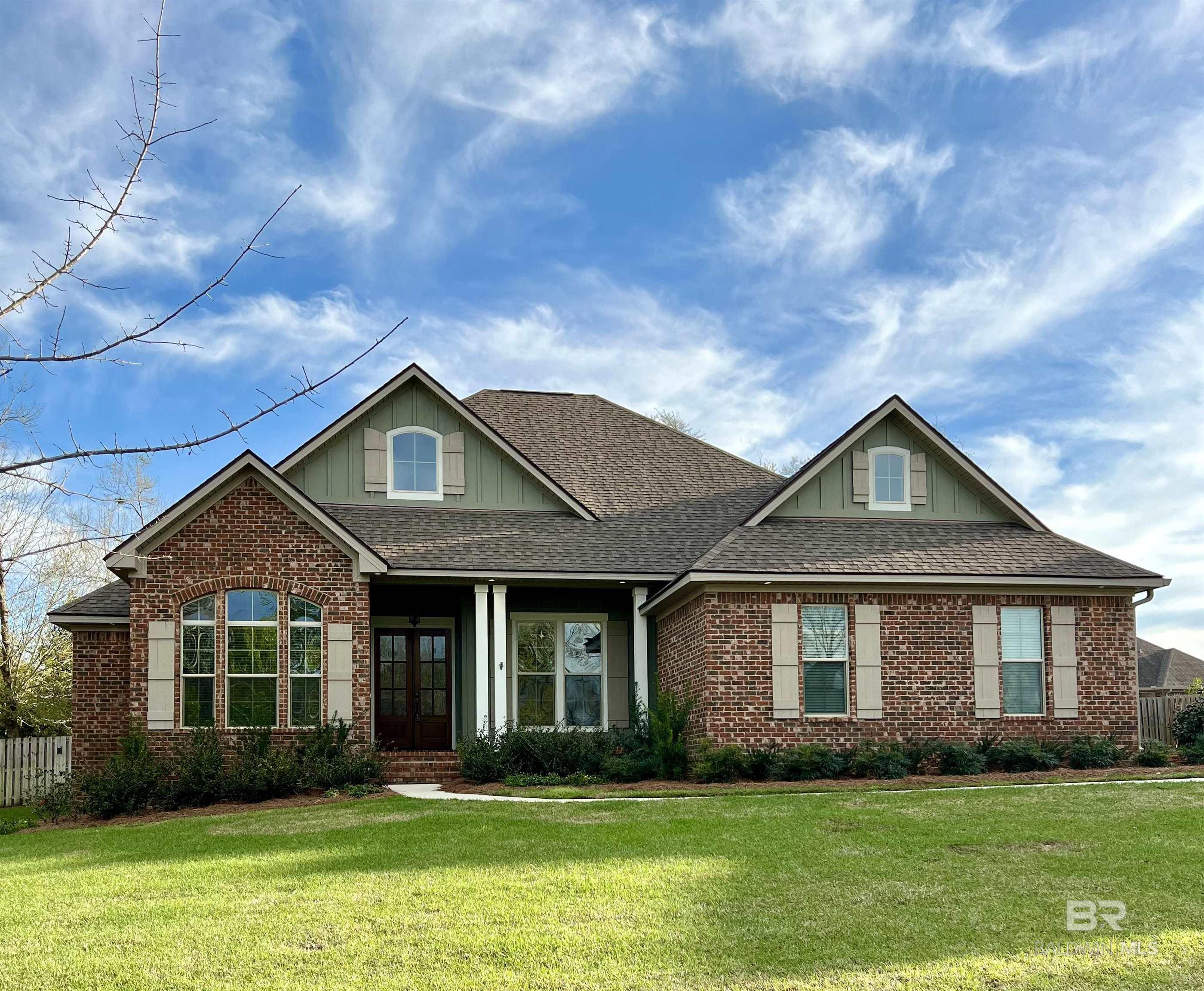 Two-story brick house with green gables, a covered entry, and a broad front lawn.
