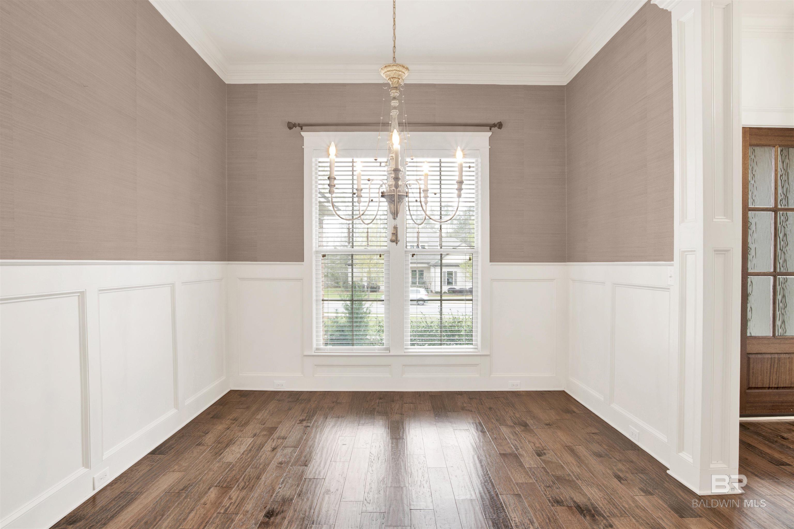 Empty dining room with chandelier, paneled wainscoting, dark wood flooring, and twin windows.