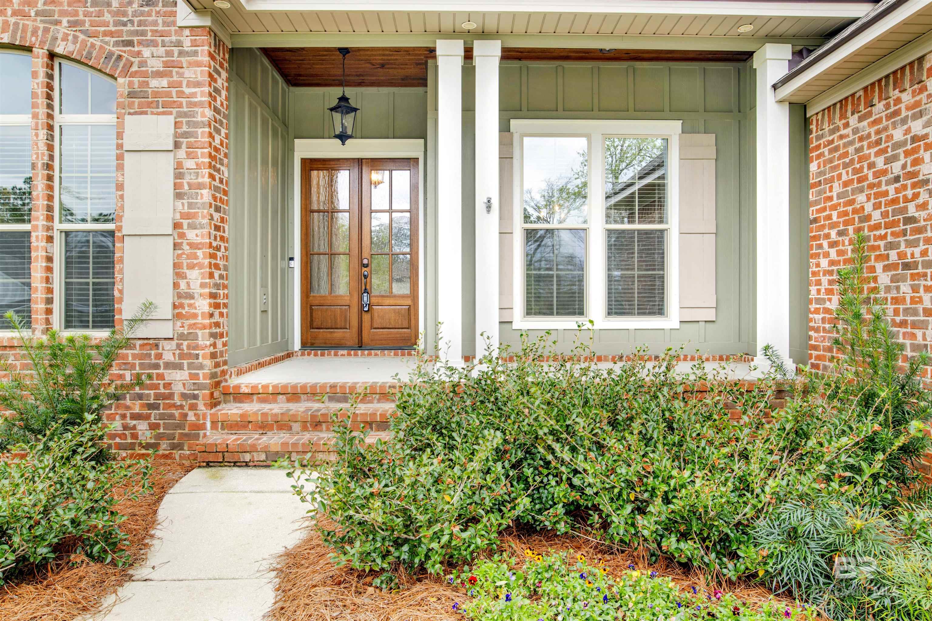 Brick house entrance with a covered porch, wooden double doors, and landscaped walkway.