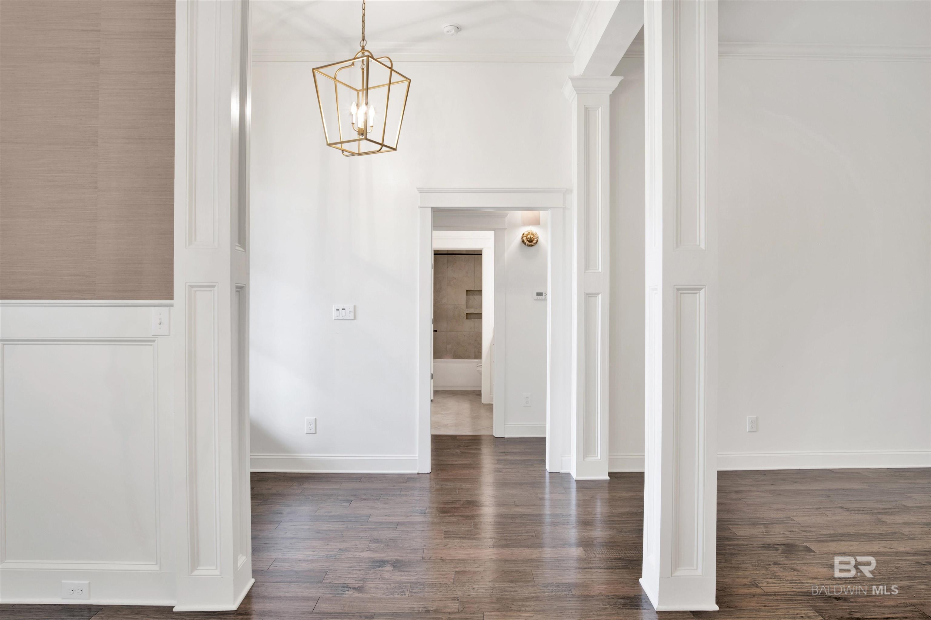 Unfurnished foyer with hardwood floors, white paneled trim, and a gold geometric pendant light.