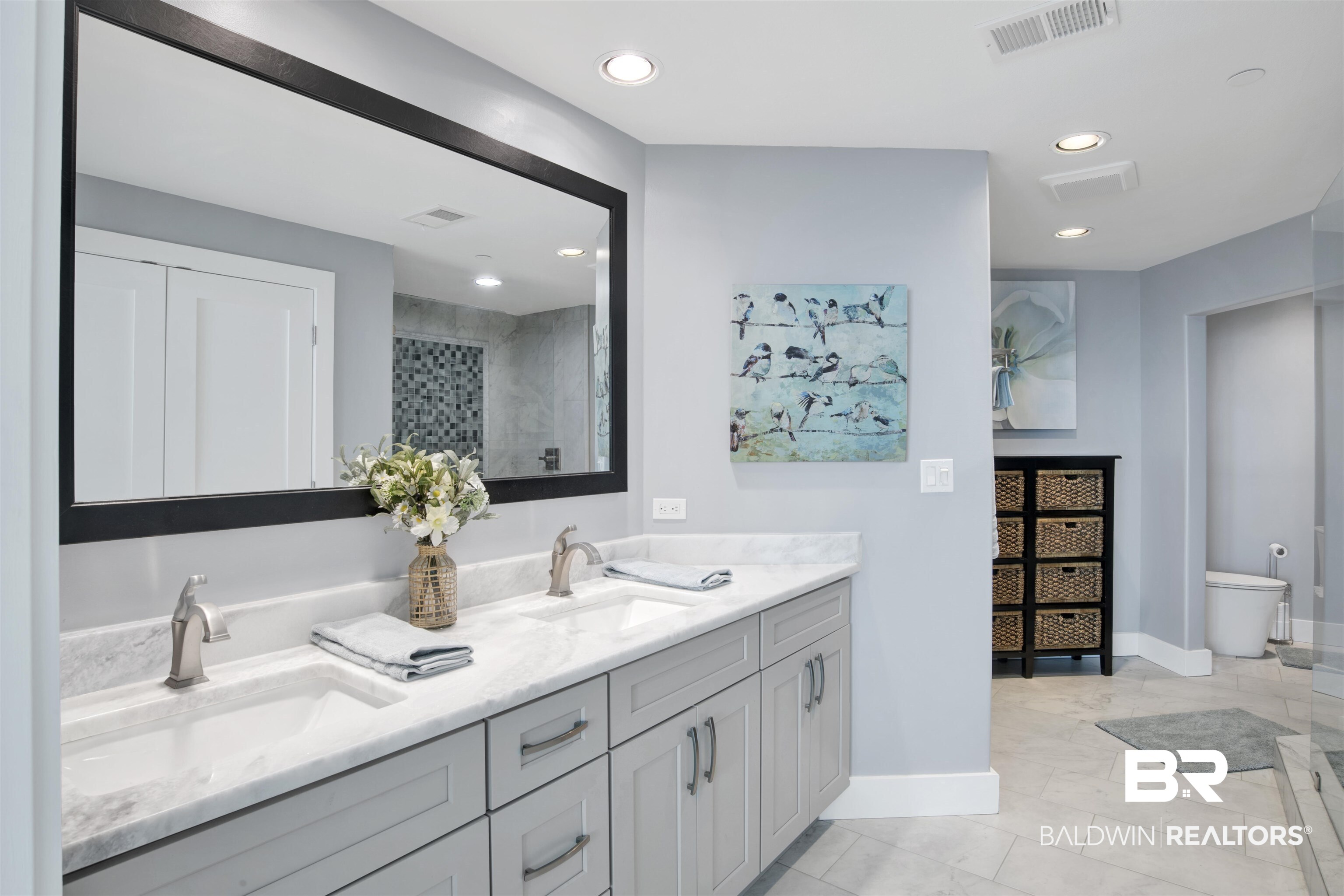 Bathroom with a double-sink vanity, marble-look counters, and a large black-framed mirror.