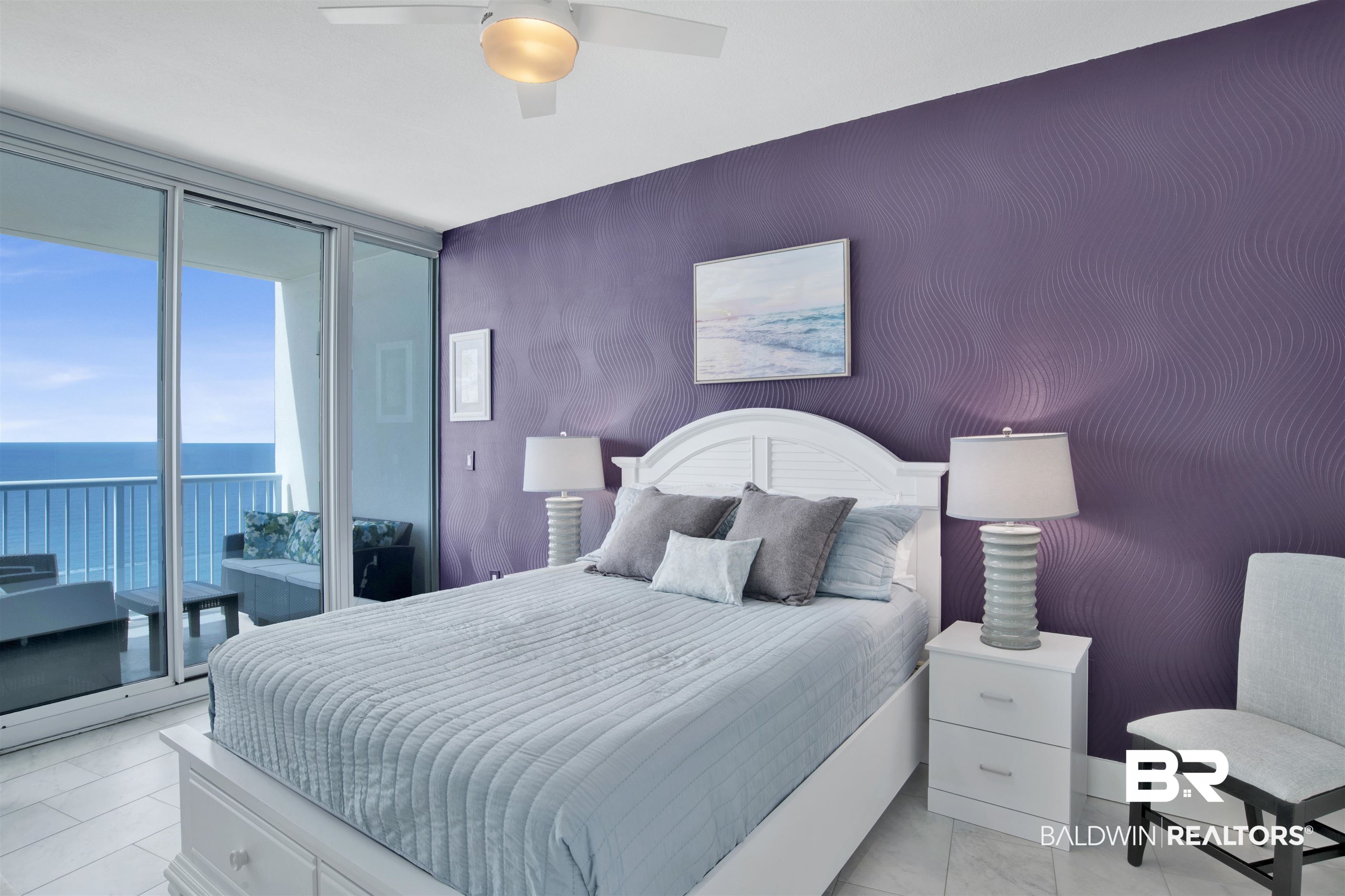 Bedroom with a white bed, purple accent wall, and sliding doors overlooking the ocean.