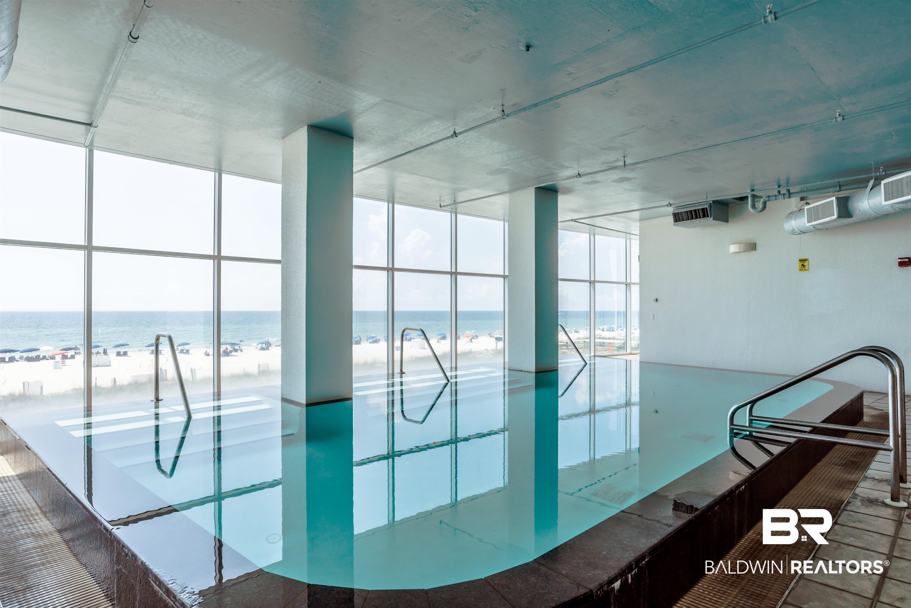 Indoor pool with floor-to-ceiling windows overlooking the beach and ocean.