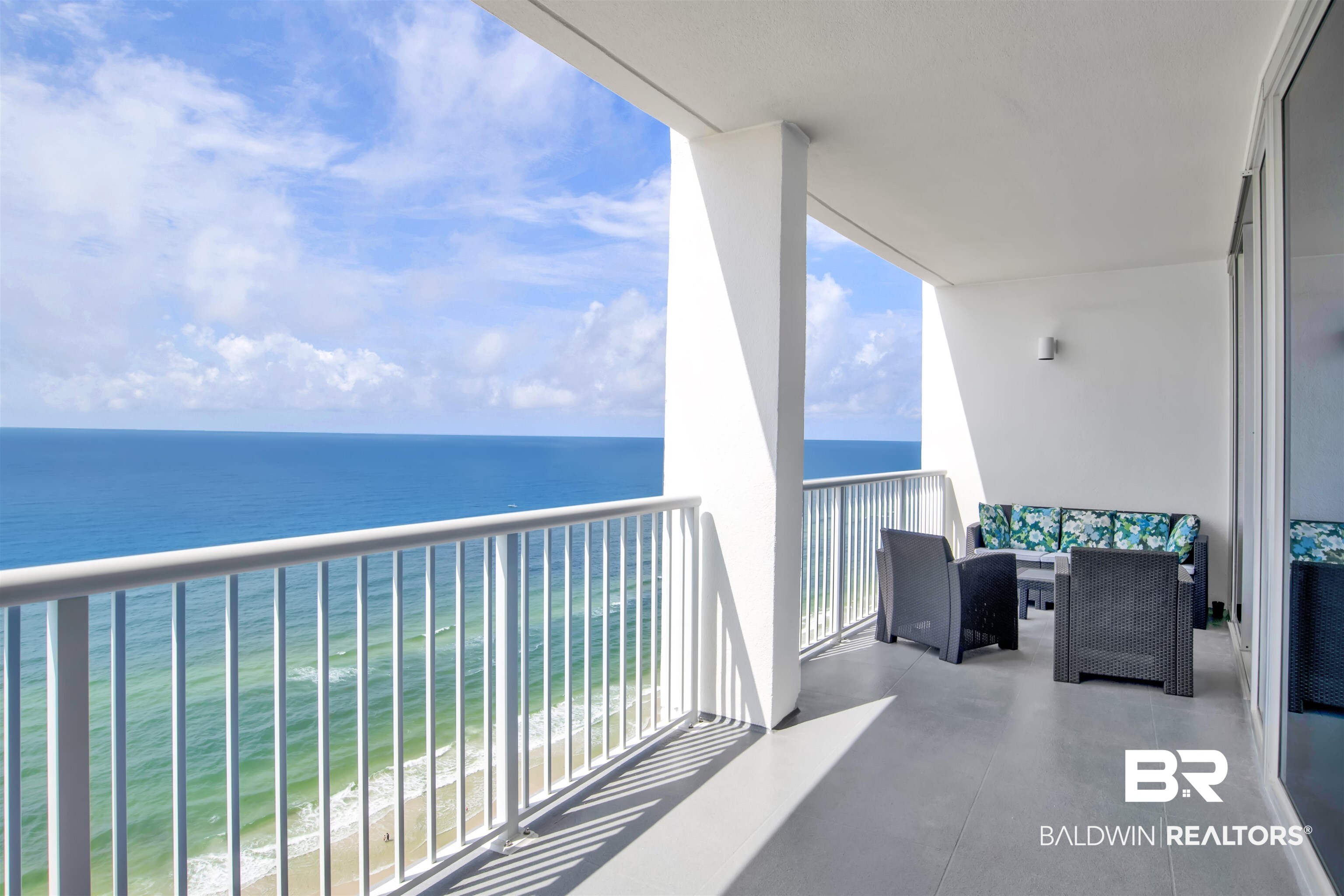 Furnished balcony overlooking the turquoise Gulf, with wicker seating and blue floral cushions.